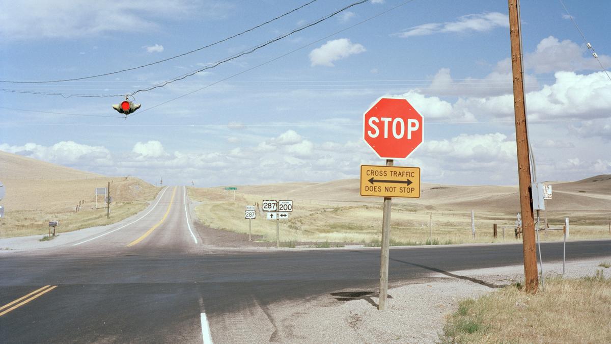 A rural road intersection with a stop sign, traffic light and highway signs under a blue sky with clouds.