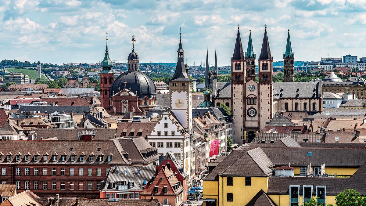 Aerial photo of Würzburg, a European cityscape with historic buildings, church spires and a clock tower under a partly cloudy sky.