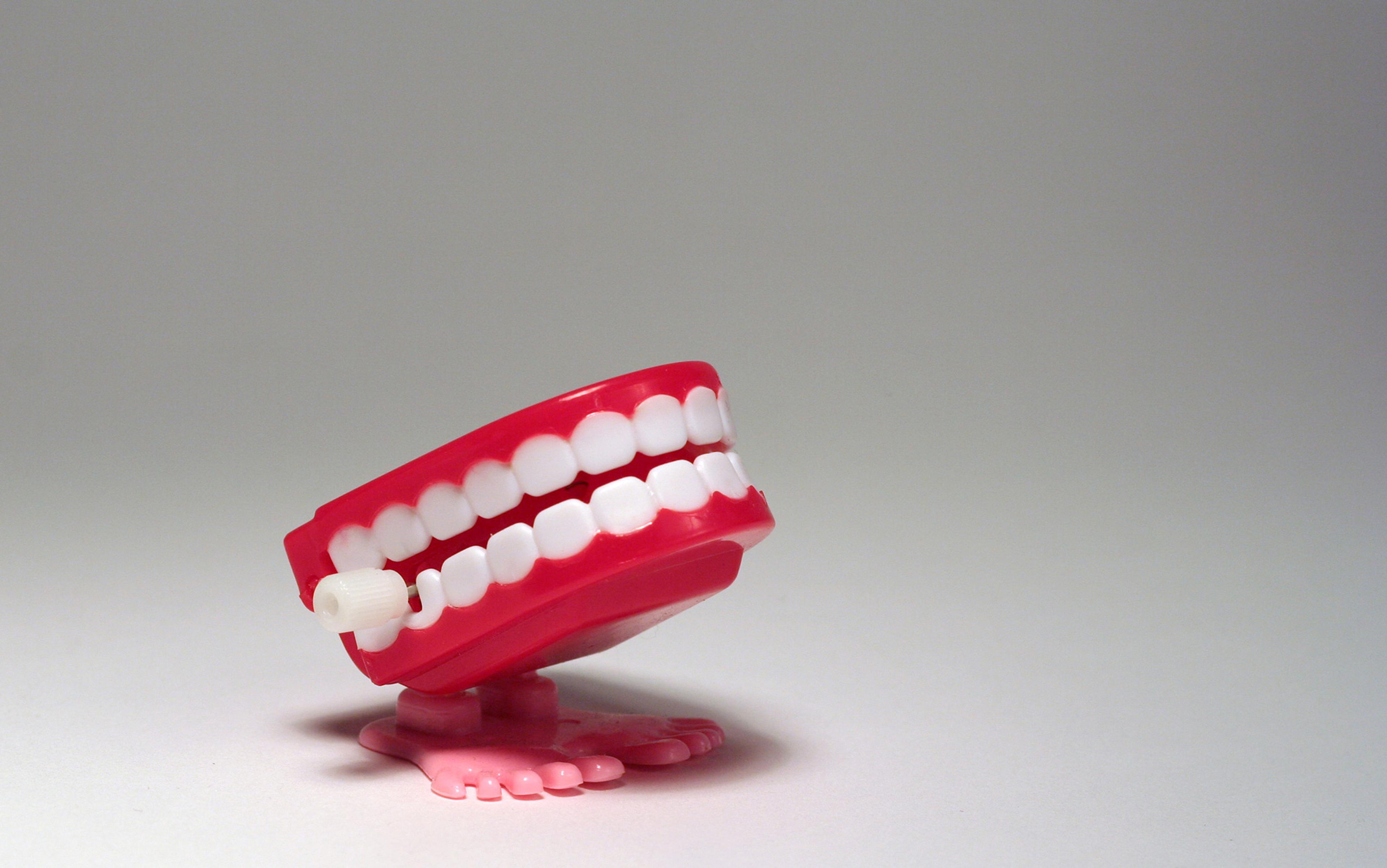 A red toy chattering teeth with white teeth and pink feet set against a plain grey background.