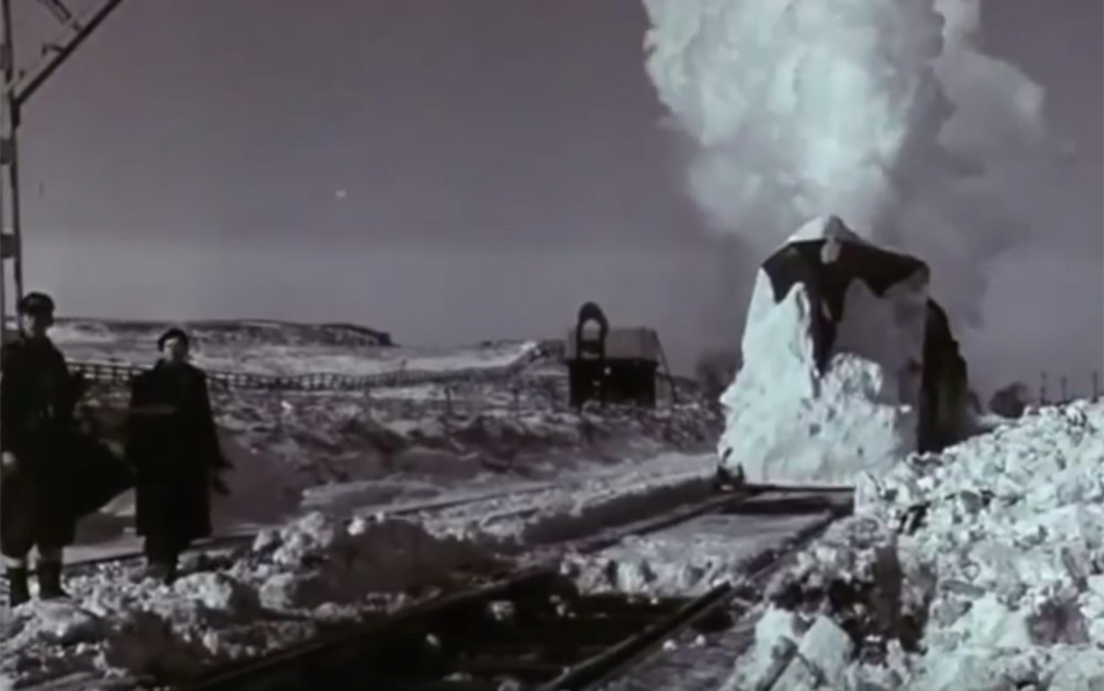 Vintage photo of a steam train clearing snow on tracks. Two people stand near the tracks in a snowy landscape.