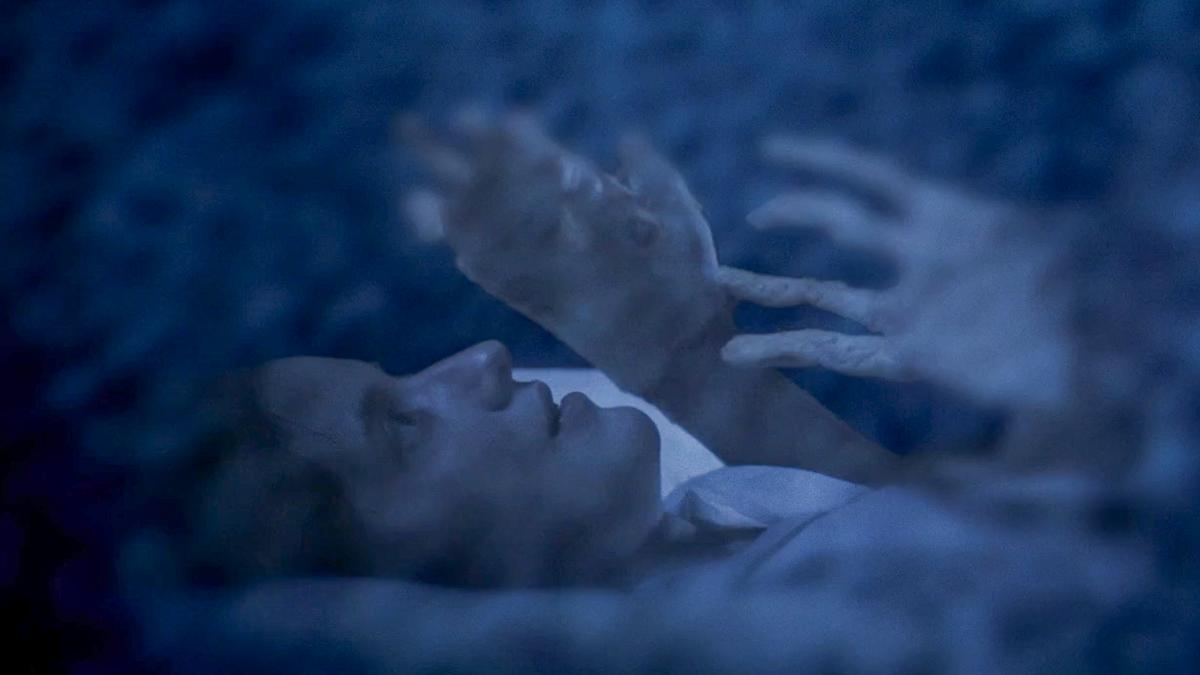 Ethereal photo of a person lying down under a blue haze with ghostly hands reaching towards them.