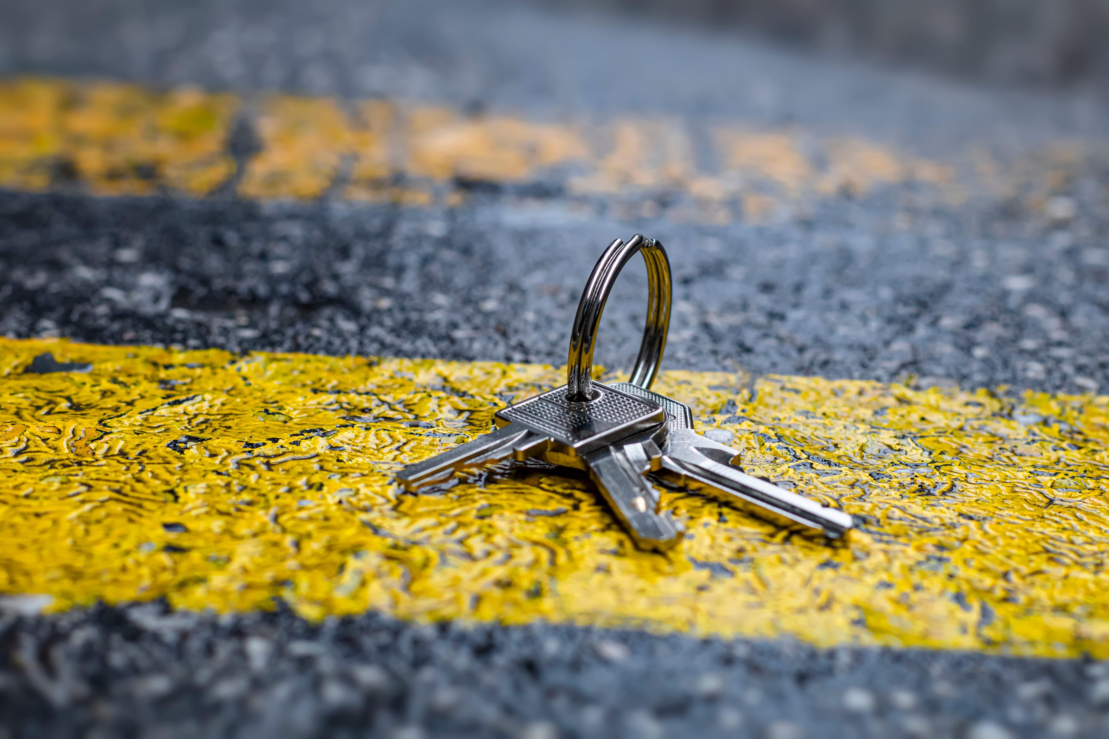 Photo of a set of keys on a pavement with yellow and grey paint markings in the background.