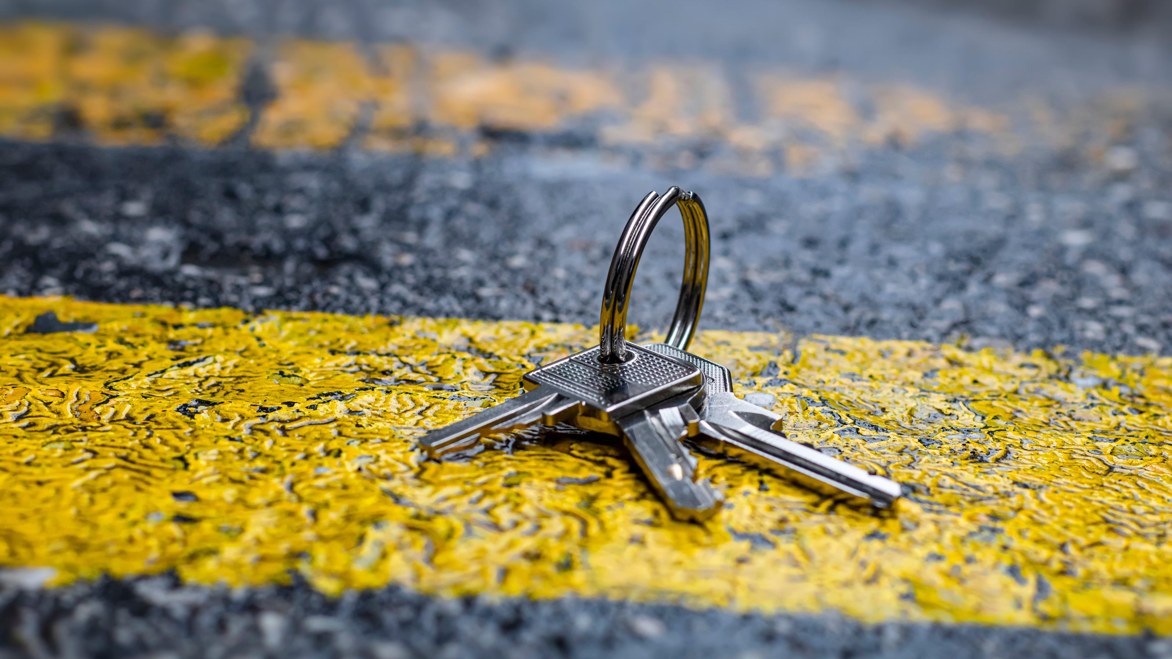 Photo of a set of keys on a pavement with yellow and grey paint markings in the background.