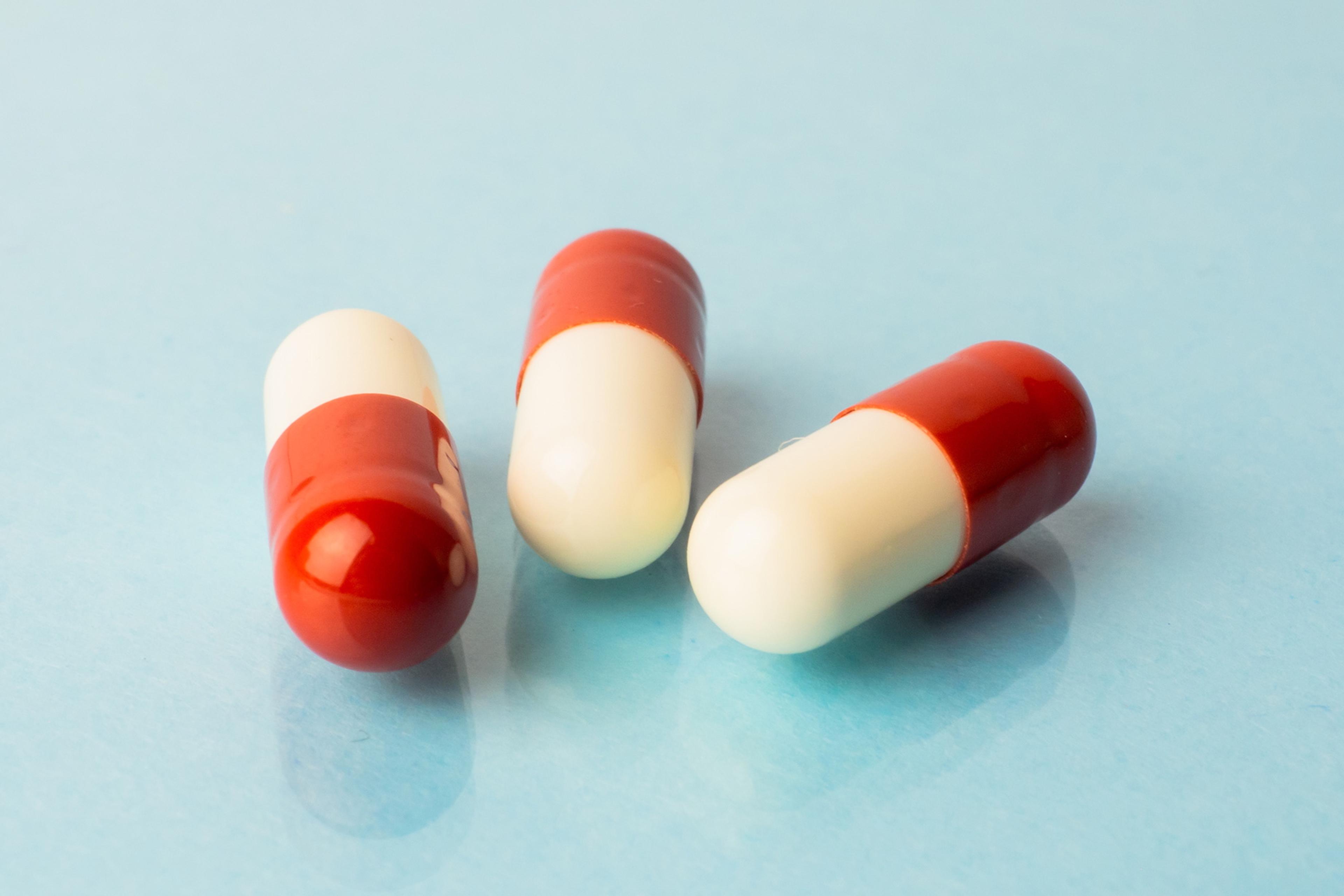 Photo of three red and white capsules on a light blue background.