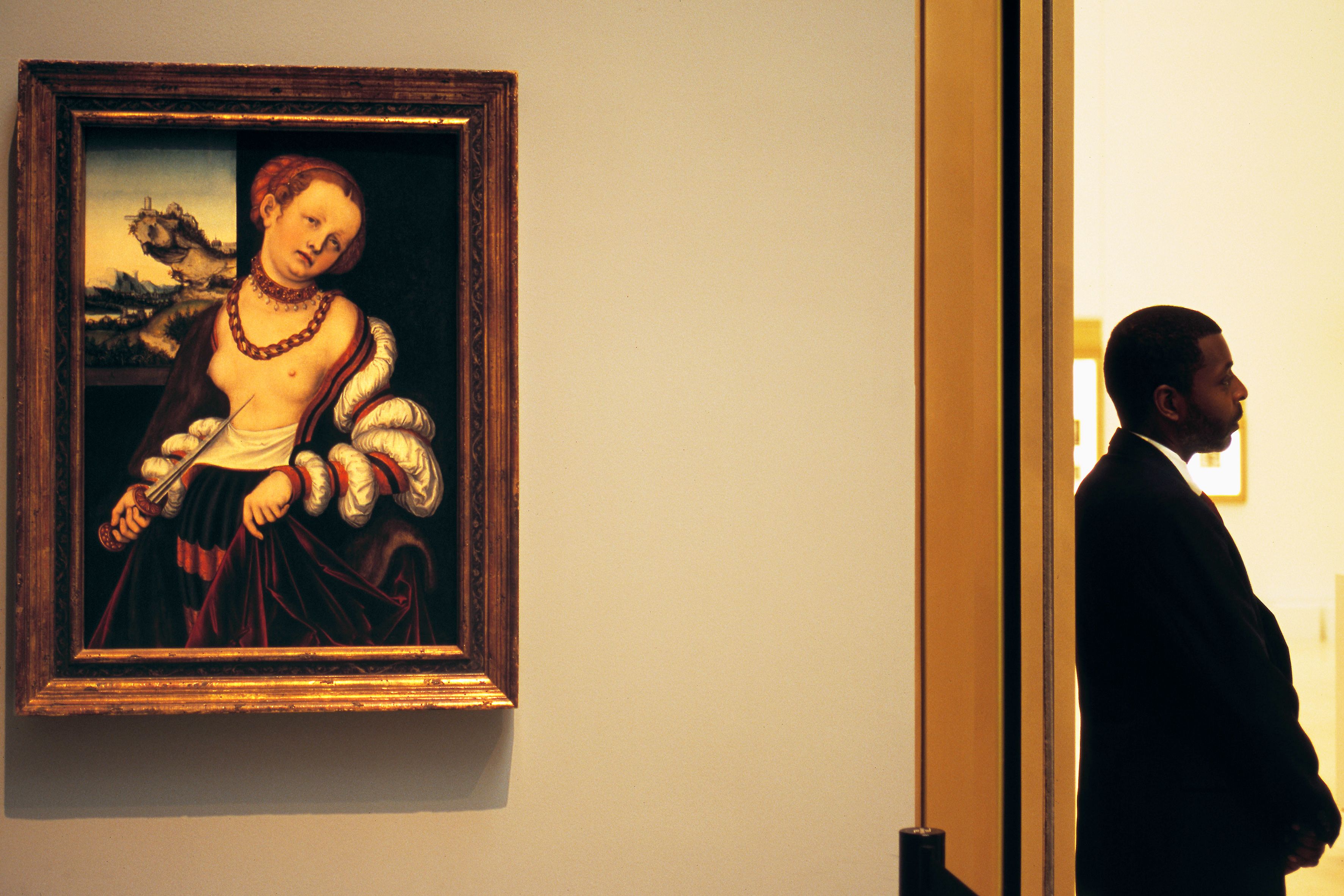 A painting on a wall with a man in a suit standing in profile beside a doorway in an art gallery.