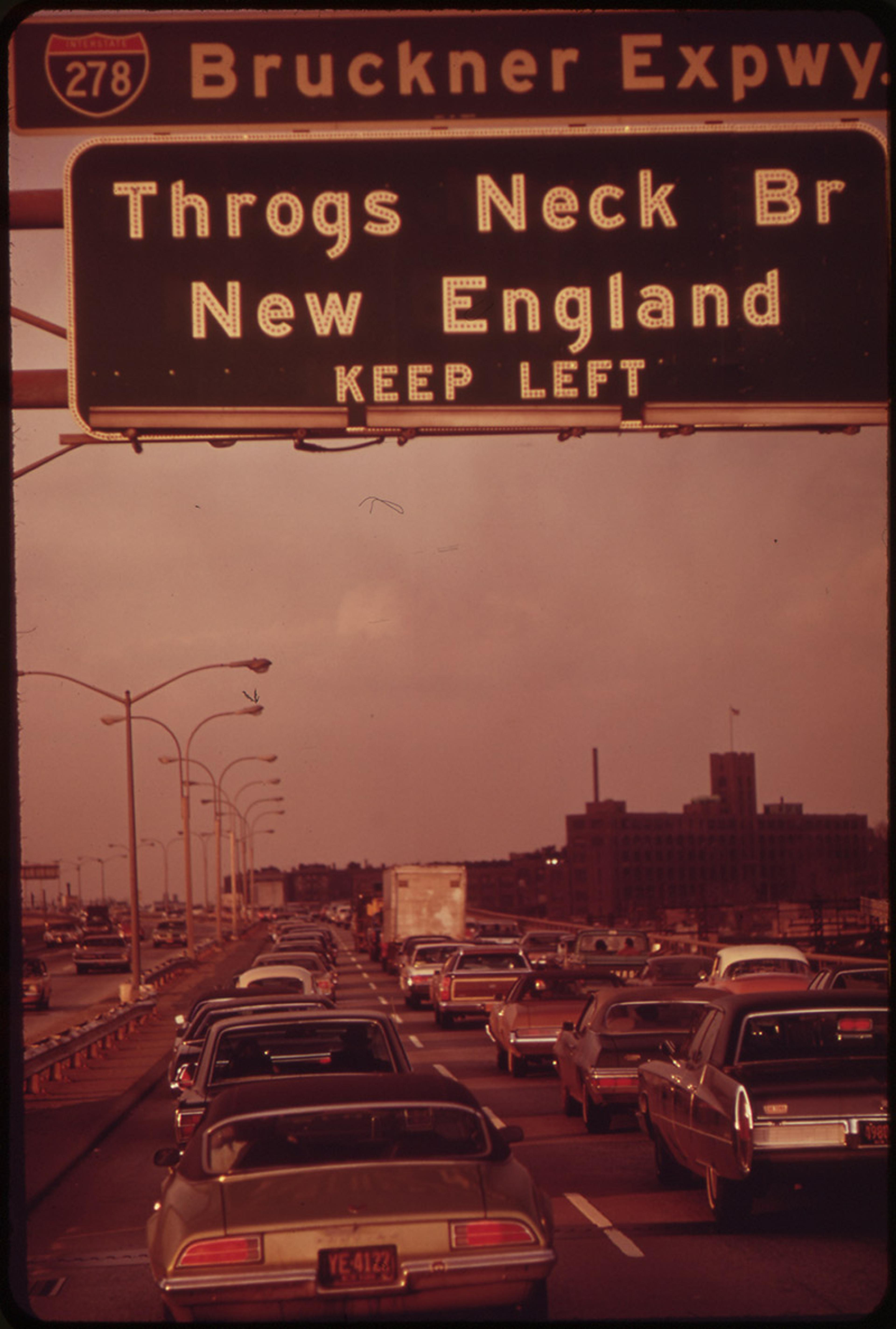 Cars in a traffic jam on the Bruckner Expressway with a road sign for Throgs Neck Bridge and New England, advising to keep left