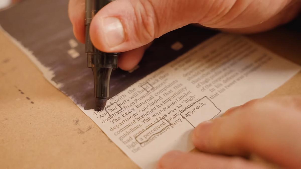 Photo of a hand using a black marker to redact text on paper several words are boxed to be emphasised.