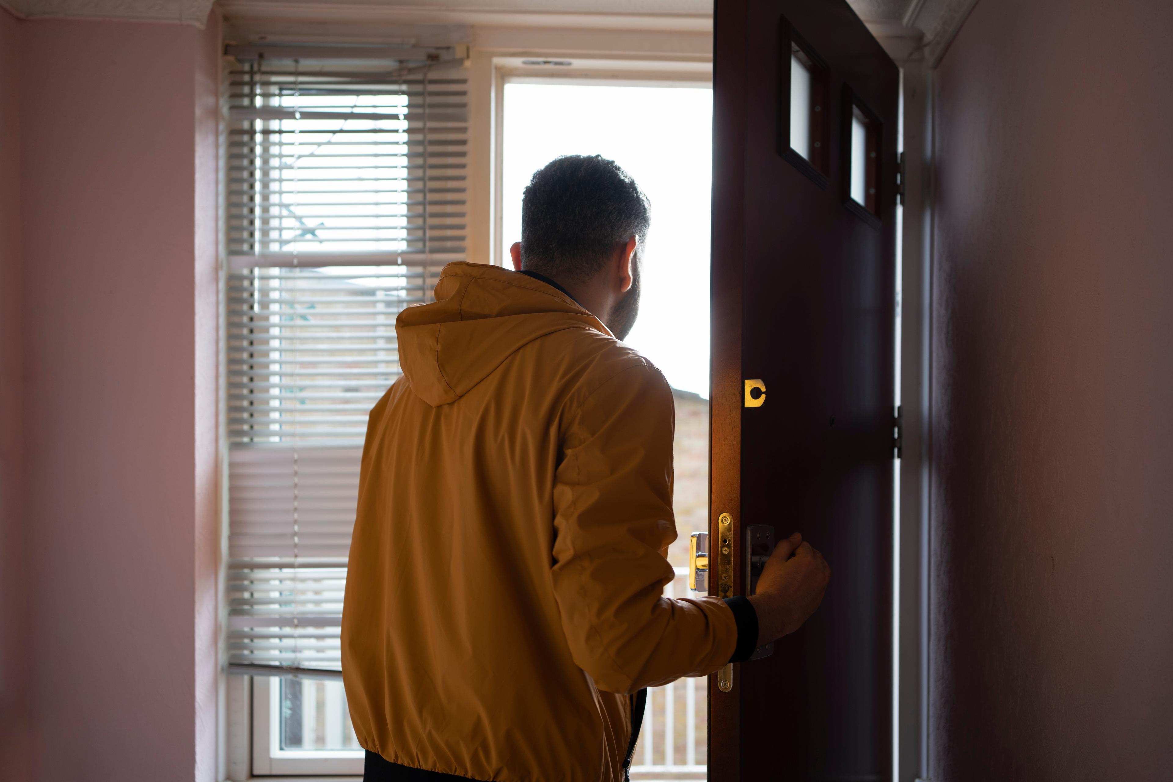 Photo of a person in a yellow jacket opening a door, facing away in a room with a window and blinds.