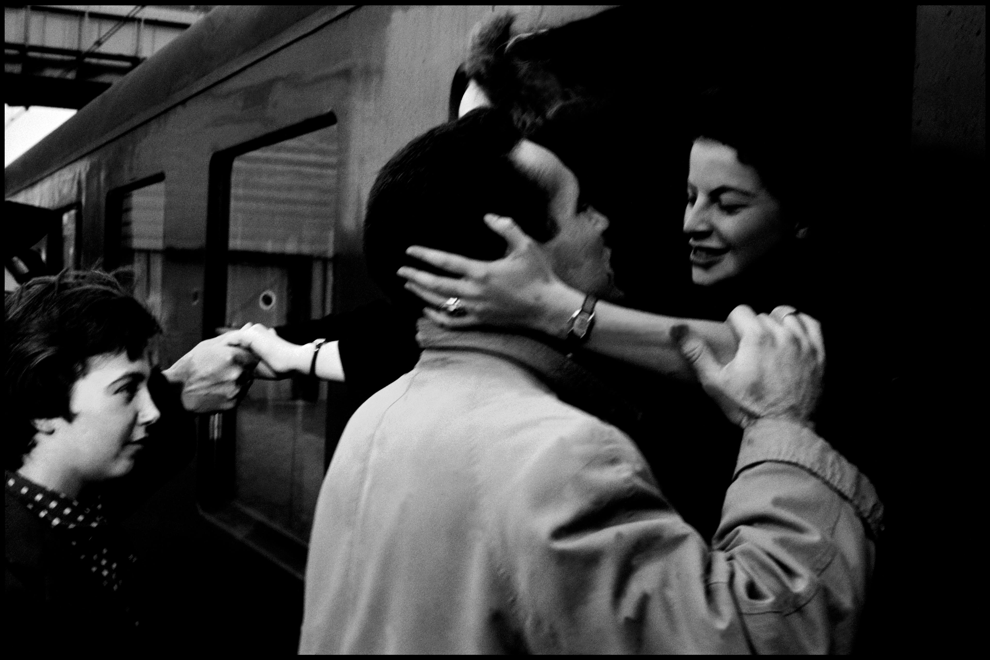 Black and white photo of people embracing and saying goodbye at a train station.