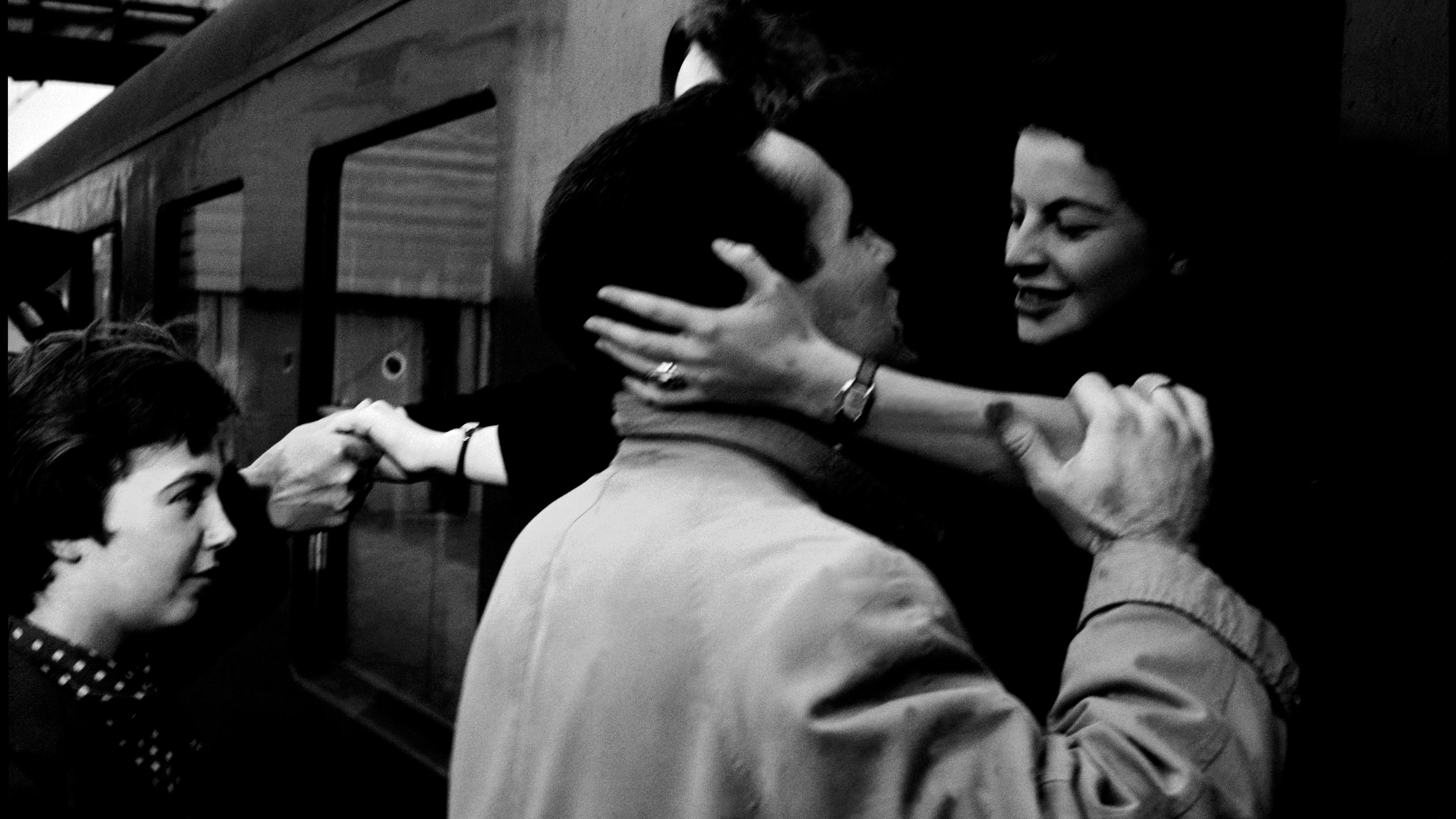 Black and white photo of people embracing and saying goodbye at a train station.