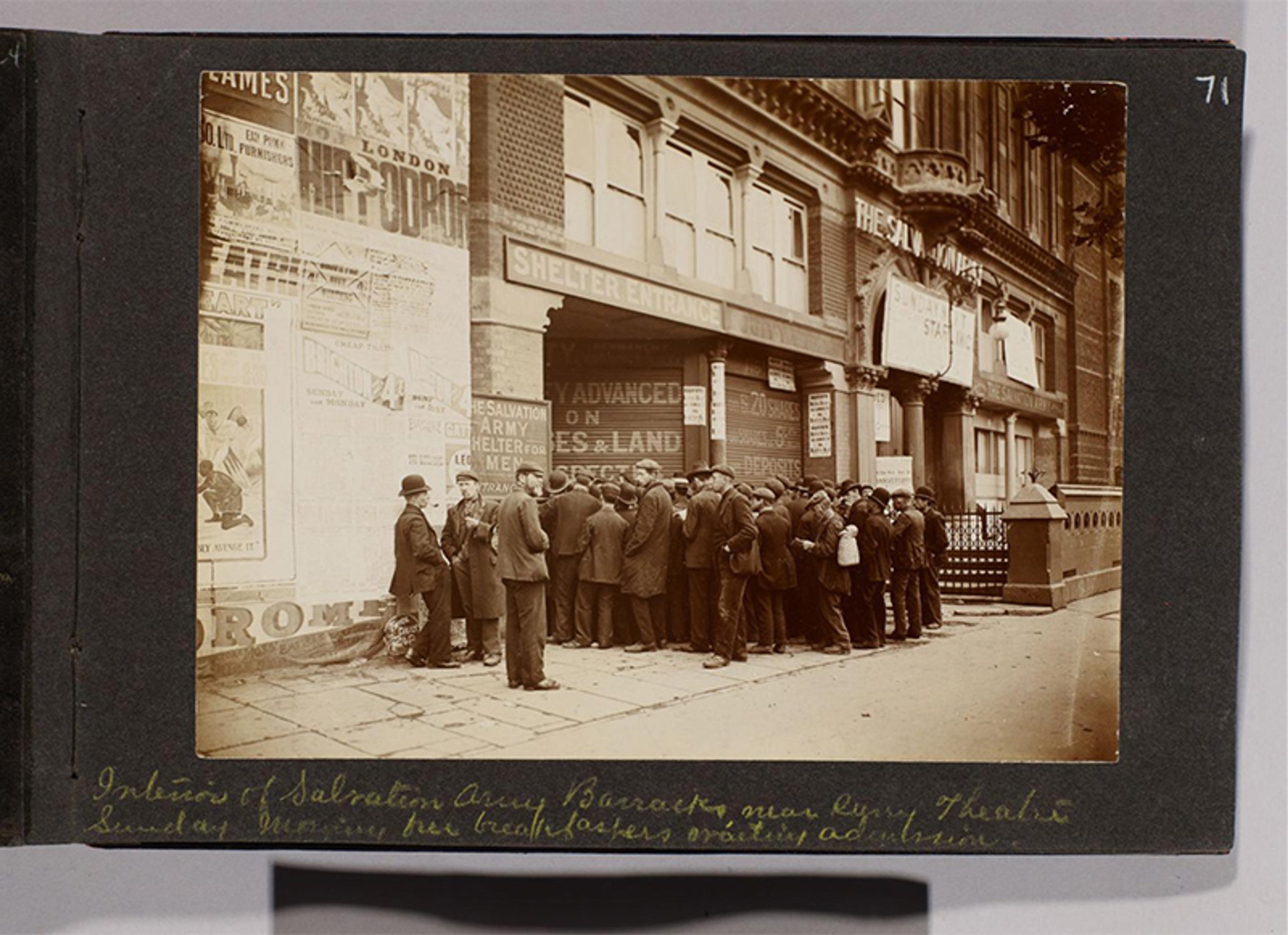 Historic photo of men queuing outside the Salvation Army Barracks near a theatre entrance, London, with posters on the wall.