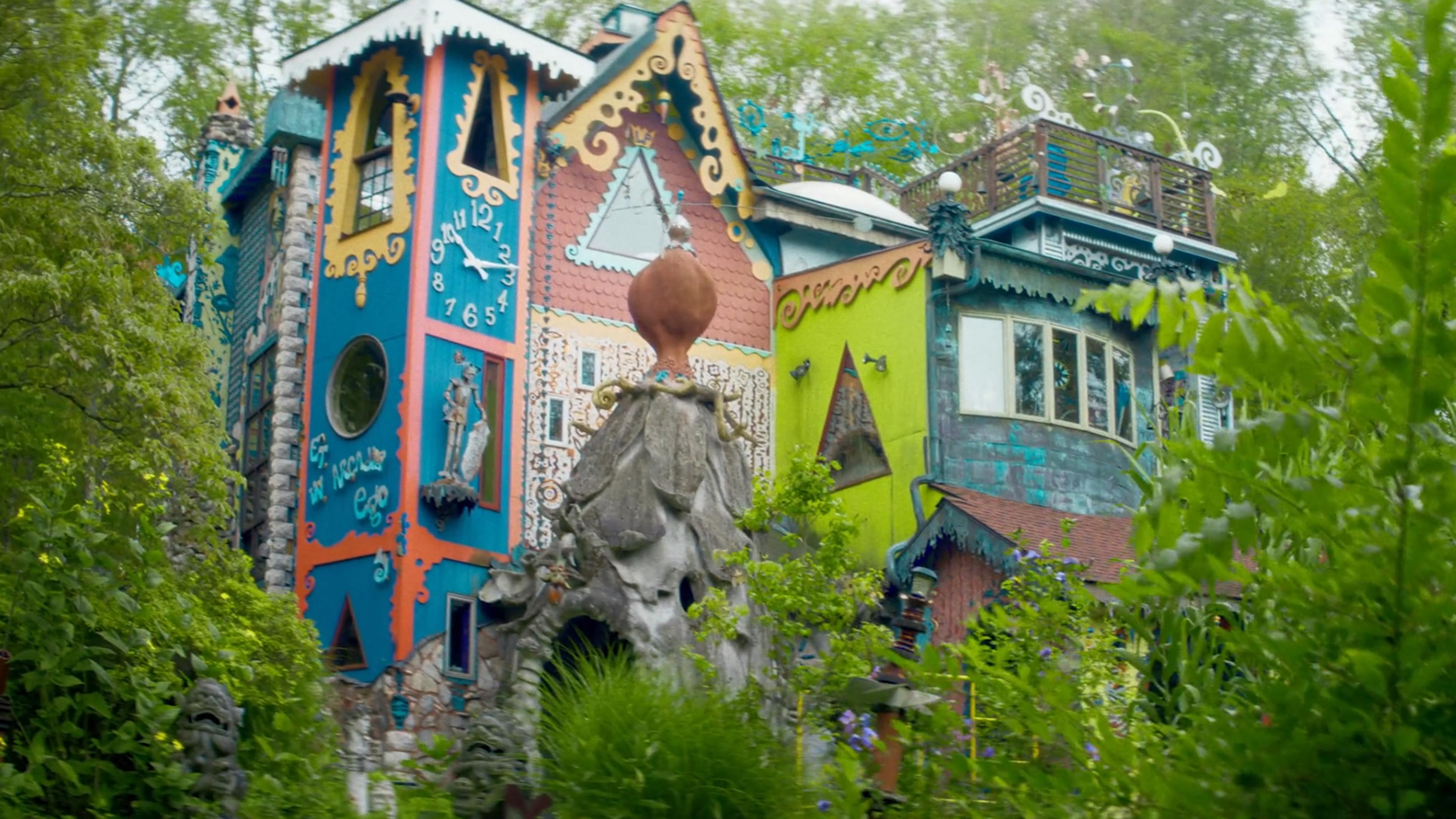 Colourful, whimsical house with ornate details and greenery in foreground, photo taken outdoors in daylight.