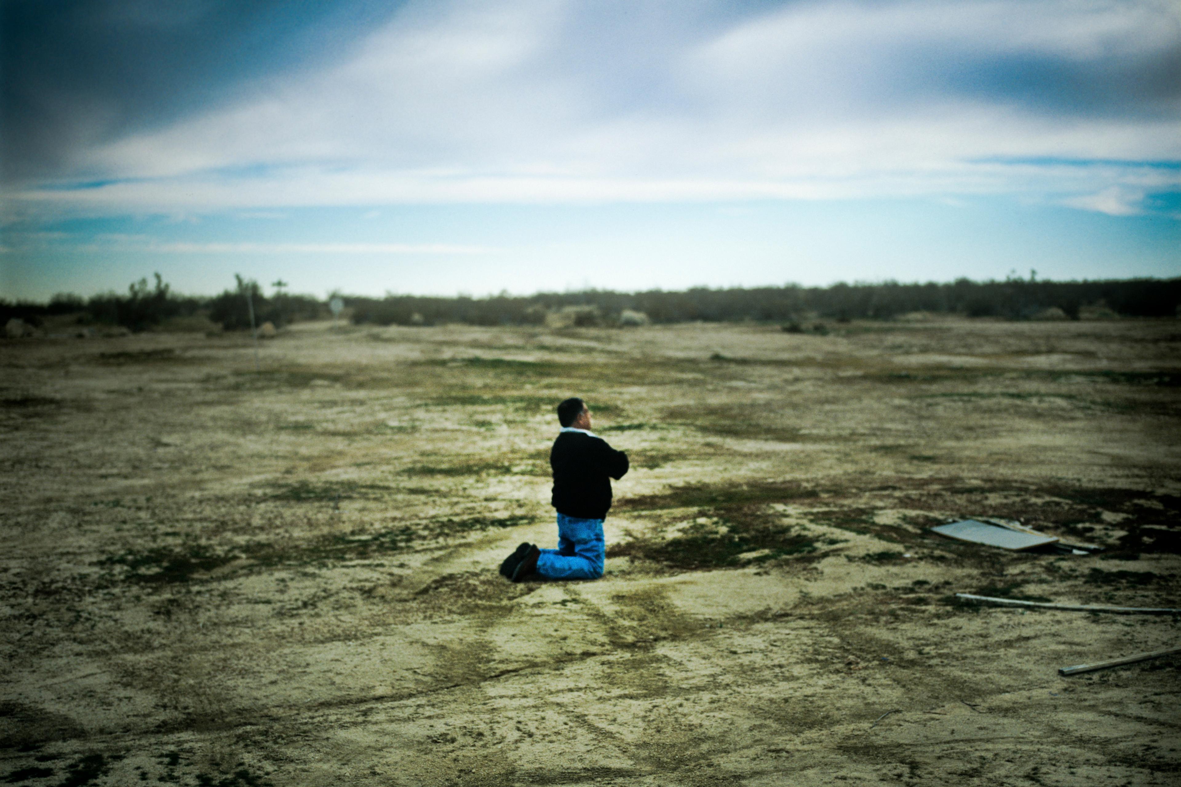 Photo of a person kneeling on a barren landscape under a cloudy sky, capturing a sense of isolation and vastness.