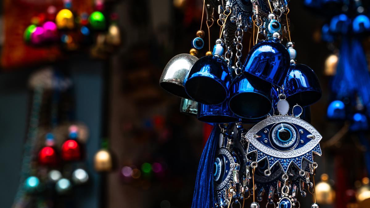 Colourful evil eye charms and blue metal bells hanging together with a blurred background.