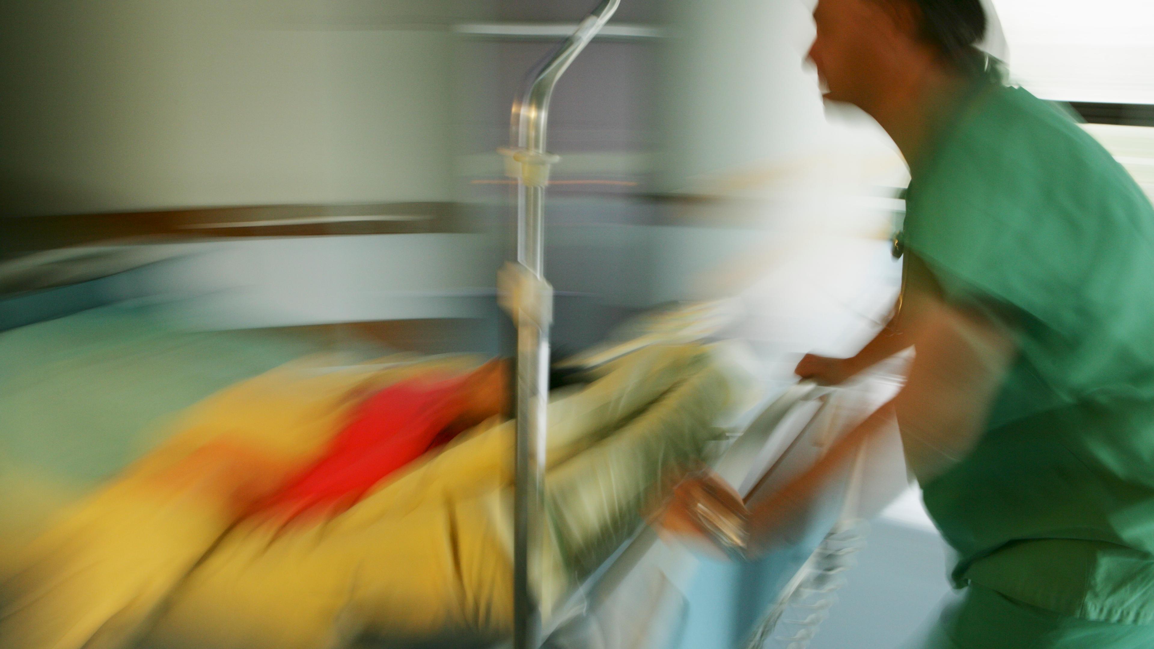 Blurred photo of a nurse in green uniform pushing a hospital gurney with a patient in a yellow blanket for urgent care.