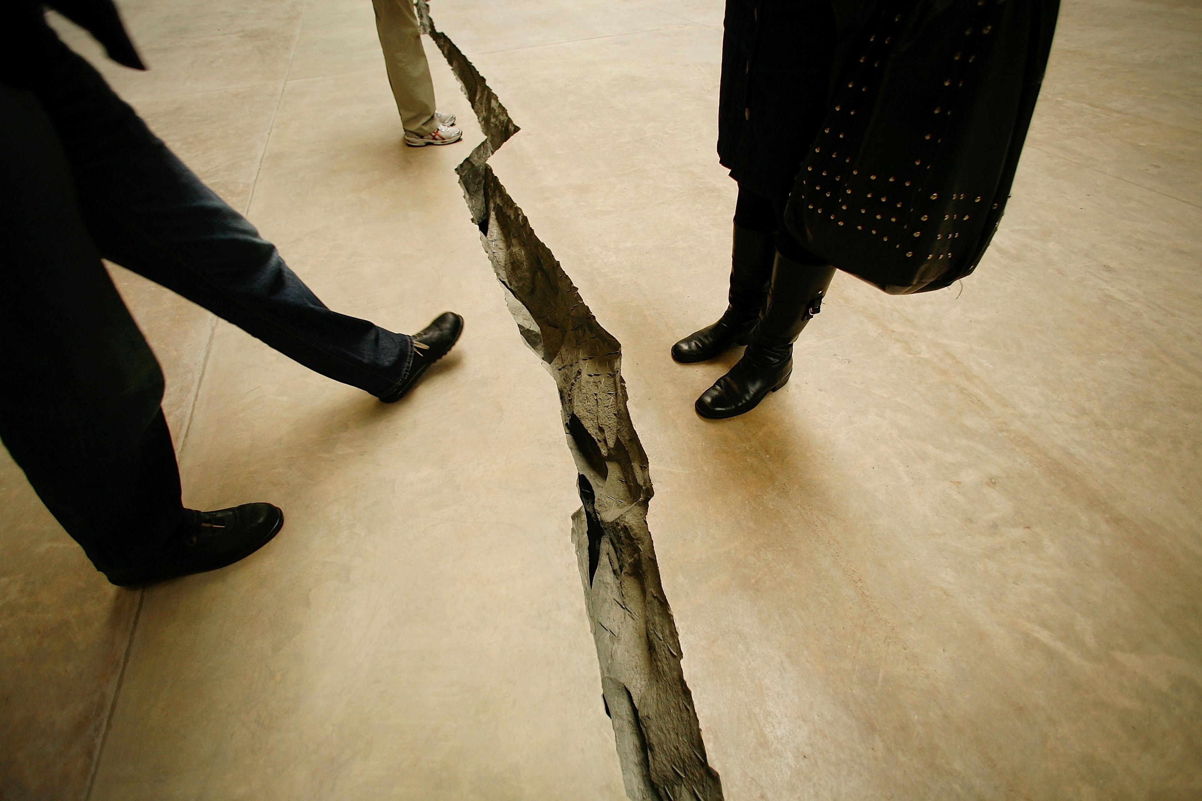 Photo of people standing near a large crack in a concrete floor, emphasising the depth and rugged edges of the split.