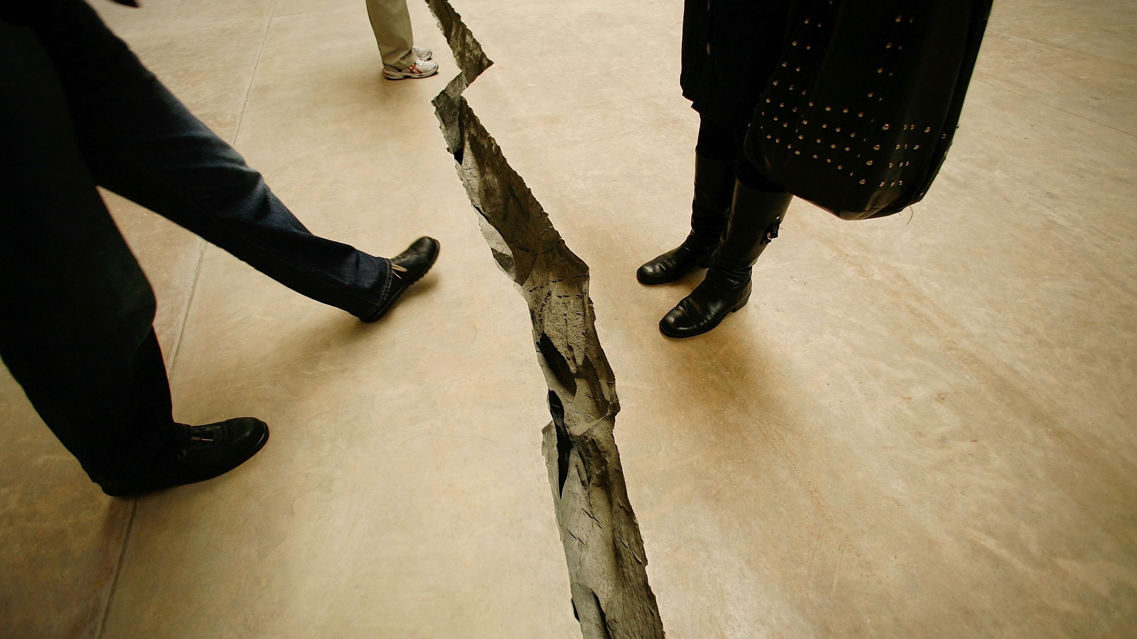 Photo of people standing near a large crack in a concrete floor, emphasising the depth and rugged edges of the split.