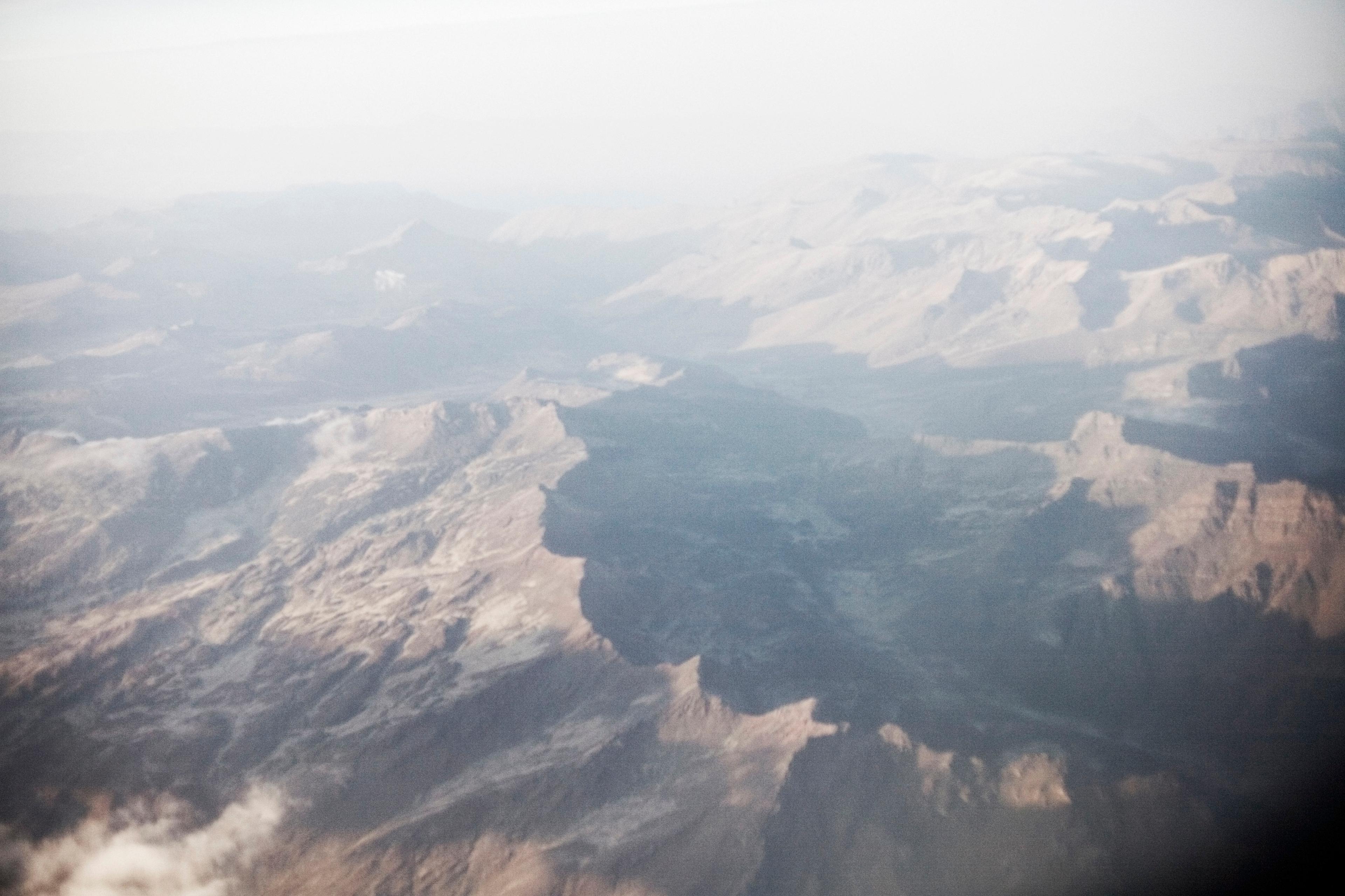 Aerial photo of a vast, misty mountain range with soft lighting and shadowed valleys in the distance.