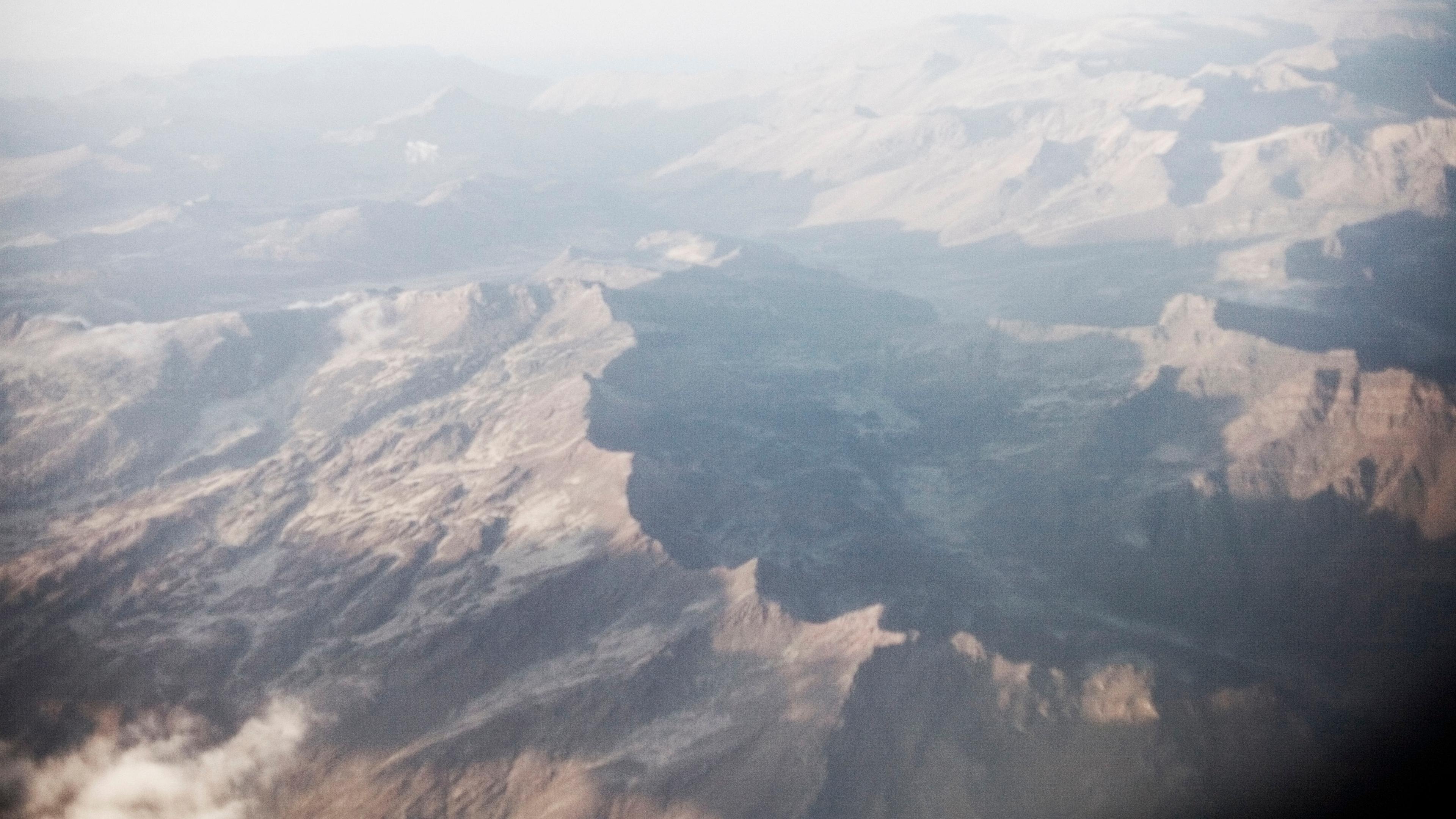 Aerial photo of a vast, misty mountain range with soft lighting and shadowed valleys in the distance.