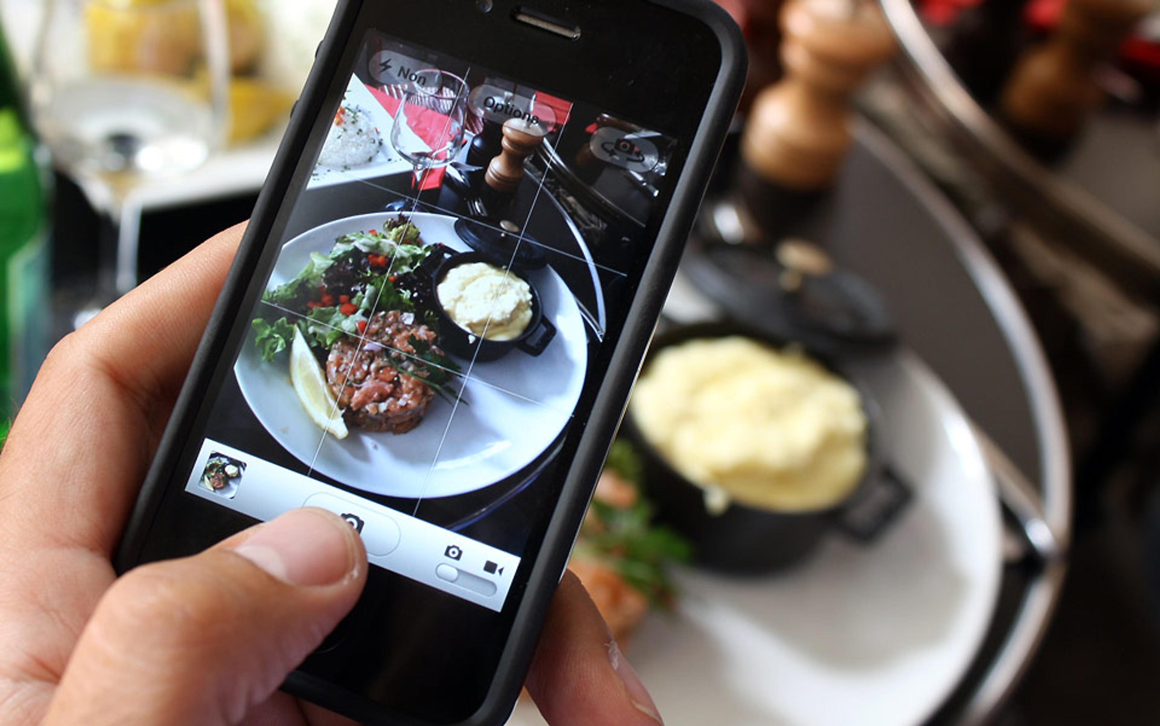 Someone taking a picture of a meal with a smartphone. The meal includes a salad, a dish of mashed potatoes, and a meat patty.