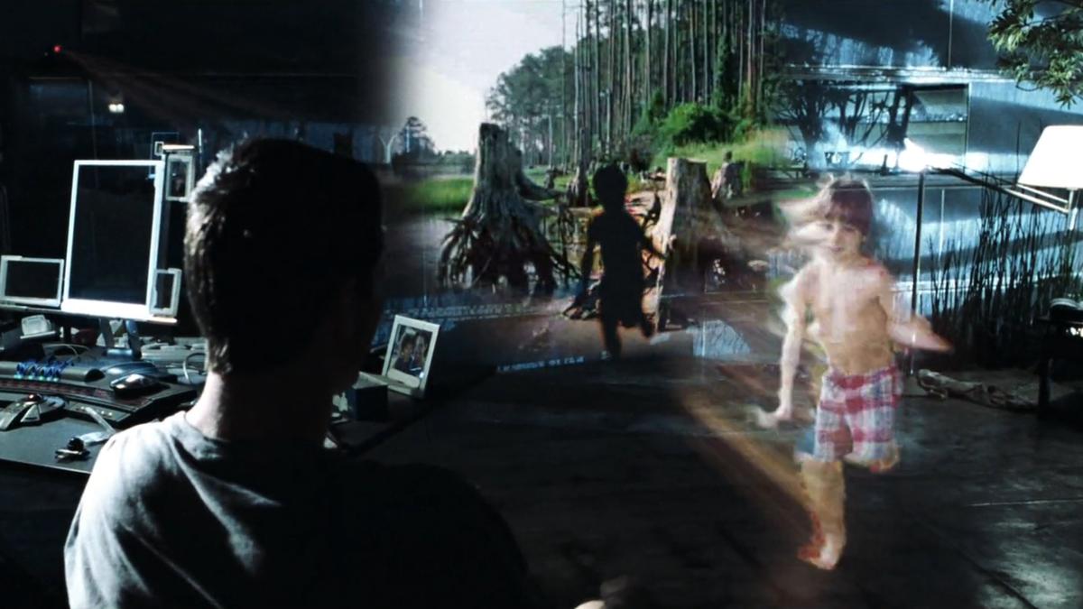 A man views a holographic projection of a child in shorts running in a forest setting; office equipment surrounds him.