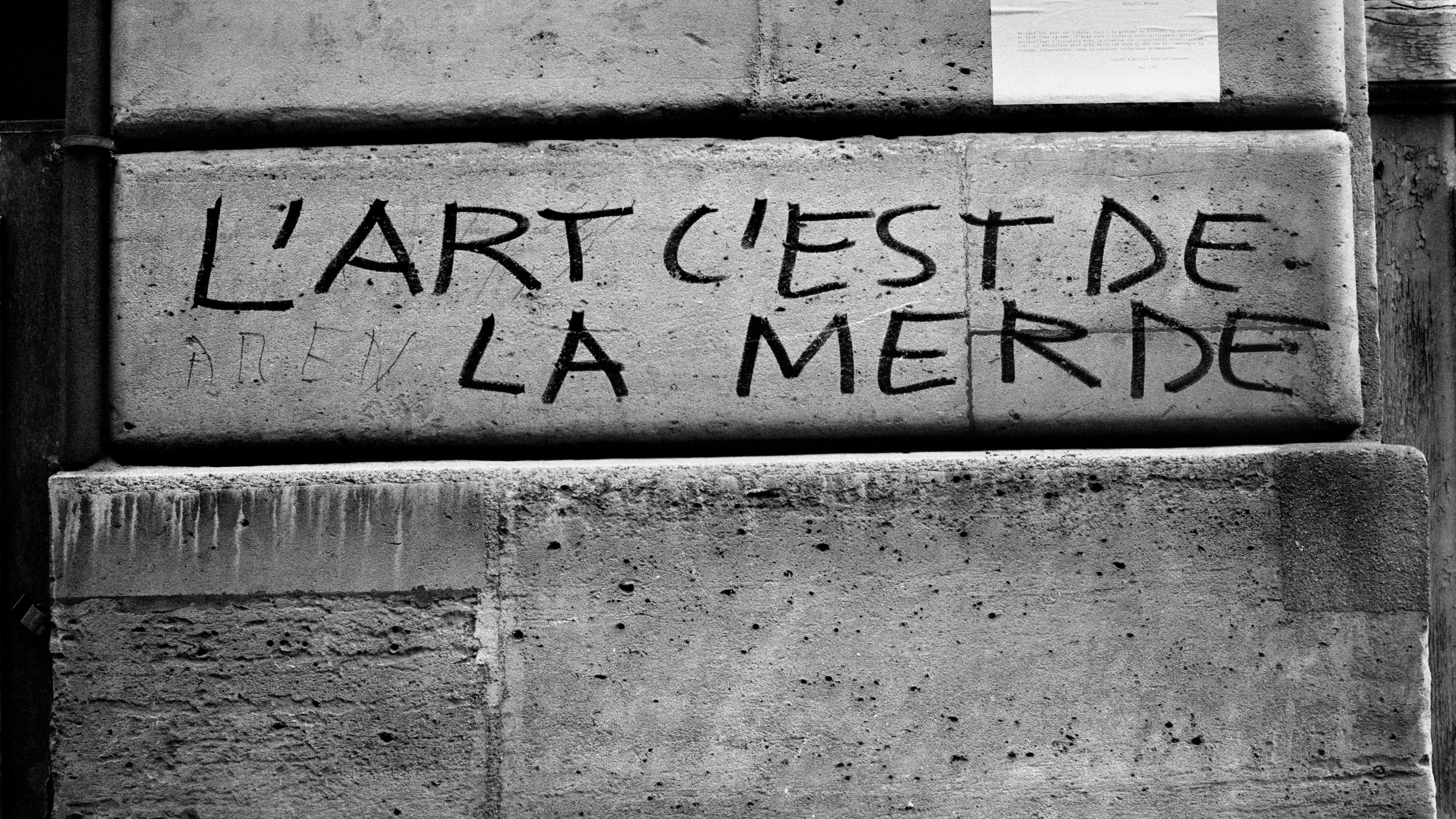 Photo of a wall with graffiti in French reading “L’art c’est de la merde” meaning “Art is shit”.