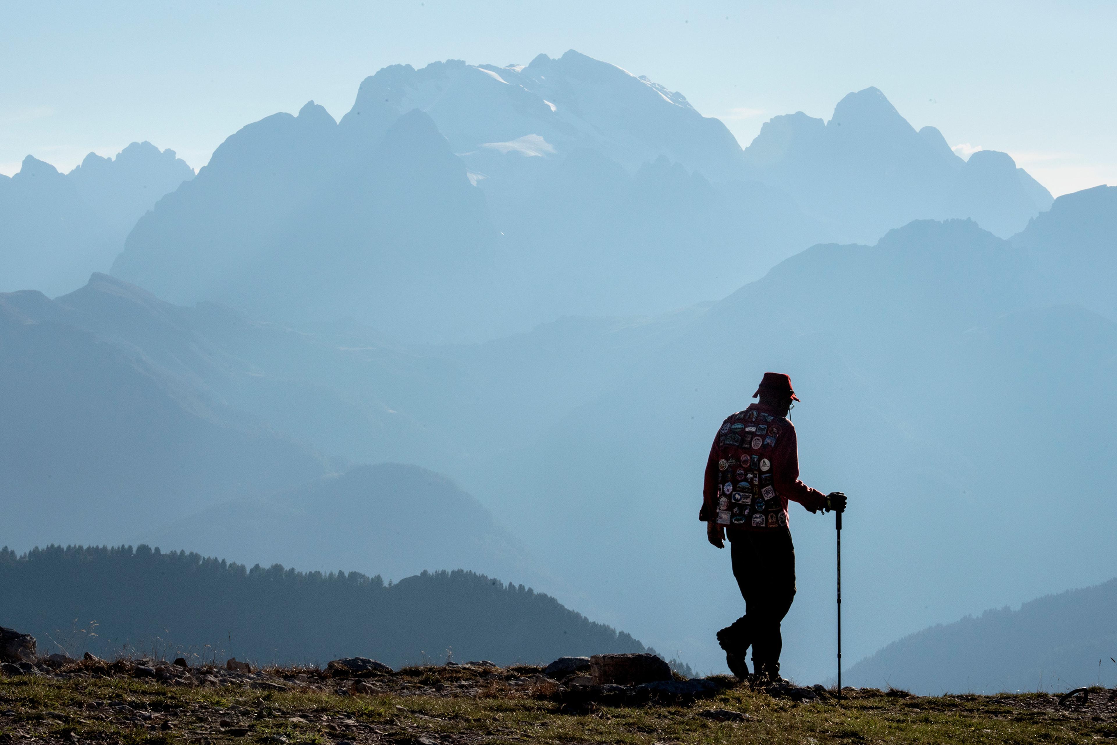 Silhouette of a hiker with a walking stick against a backdrop of layered mountains on a clear day; photo.