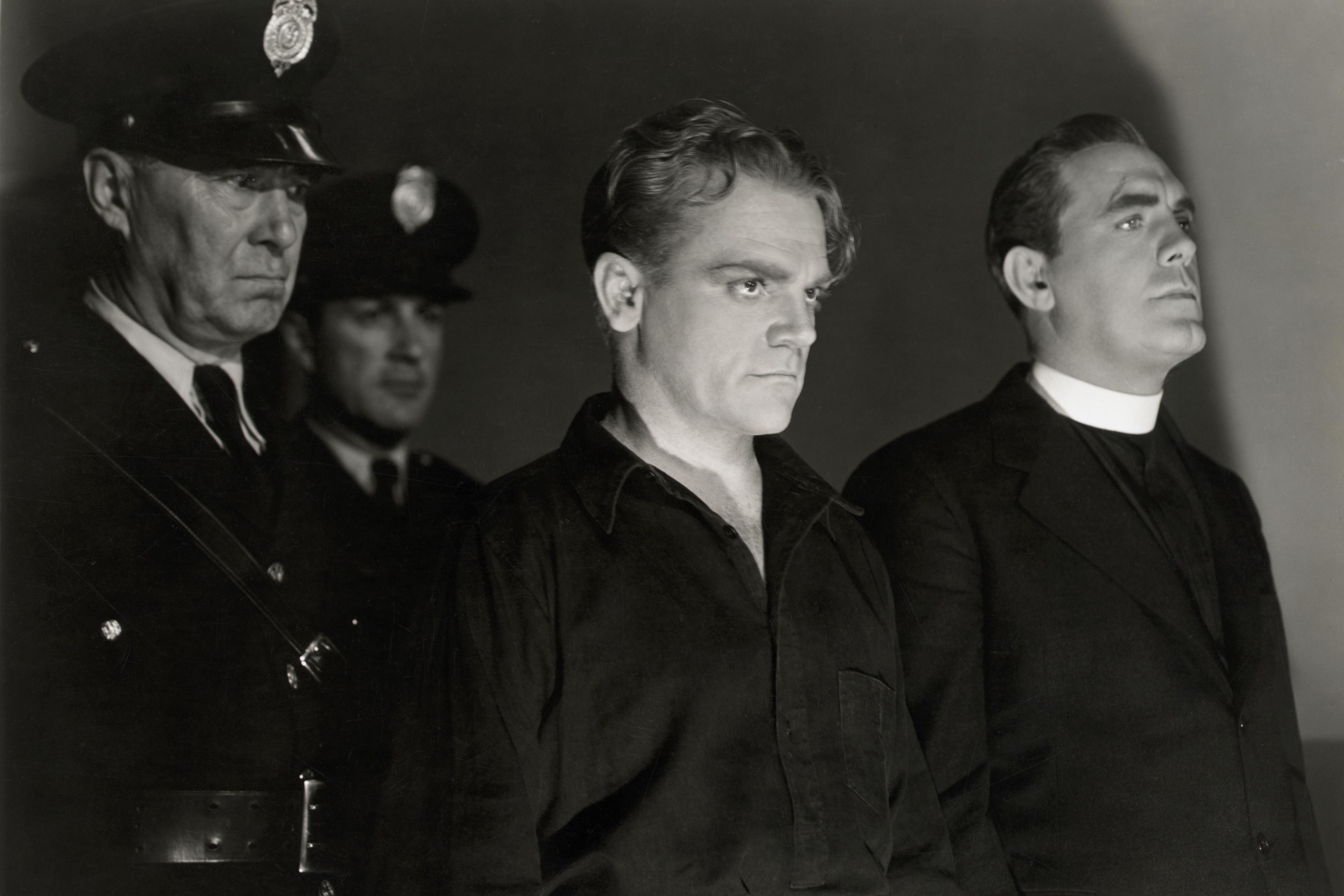 Black and white photo of two policemen, a man in dark clothing, and a priest standing in a dimly lit setting.