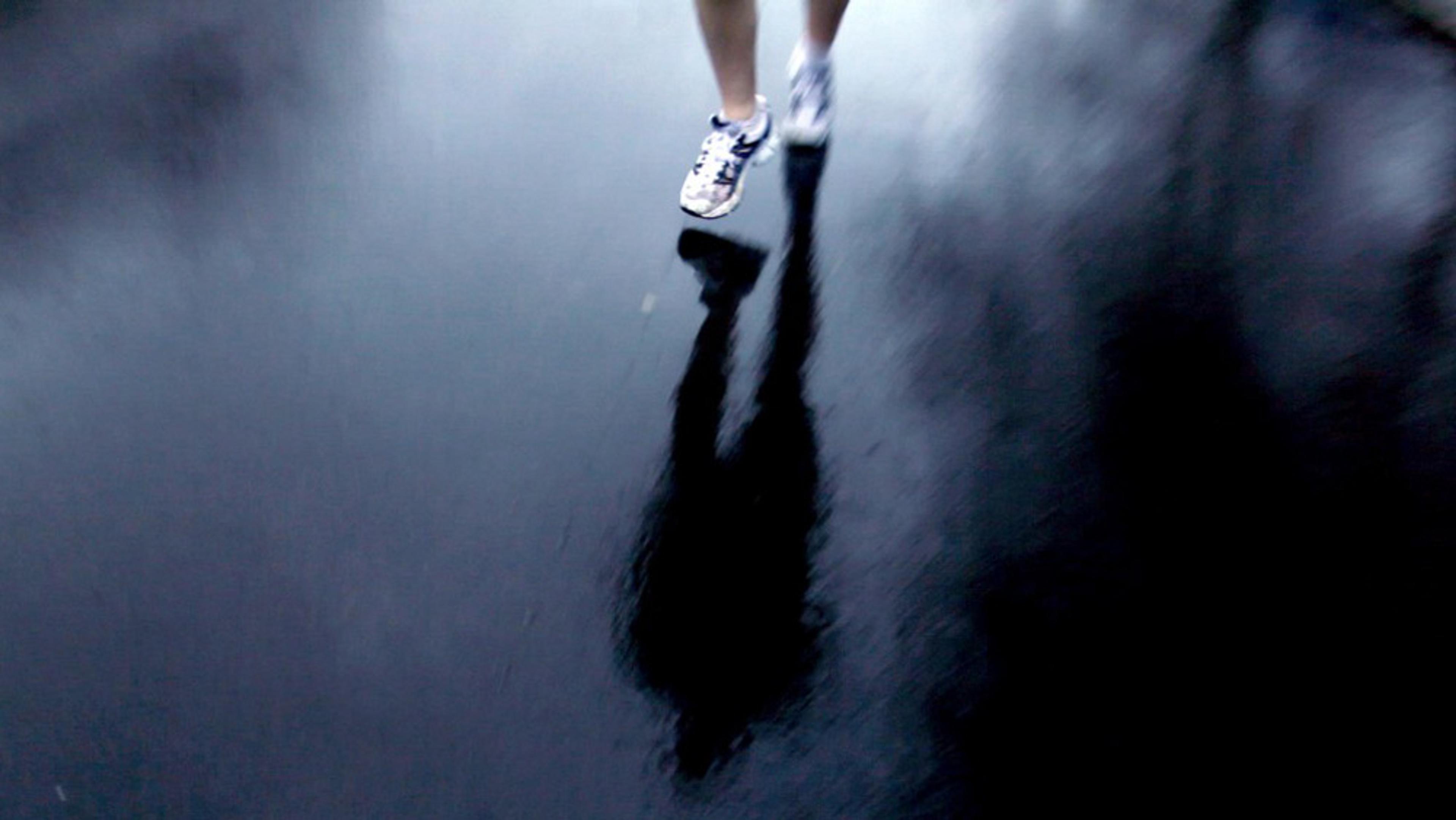 A blurred person jogging on a wet pavement, reflecting their legs and shoes.