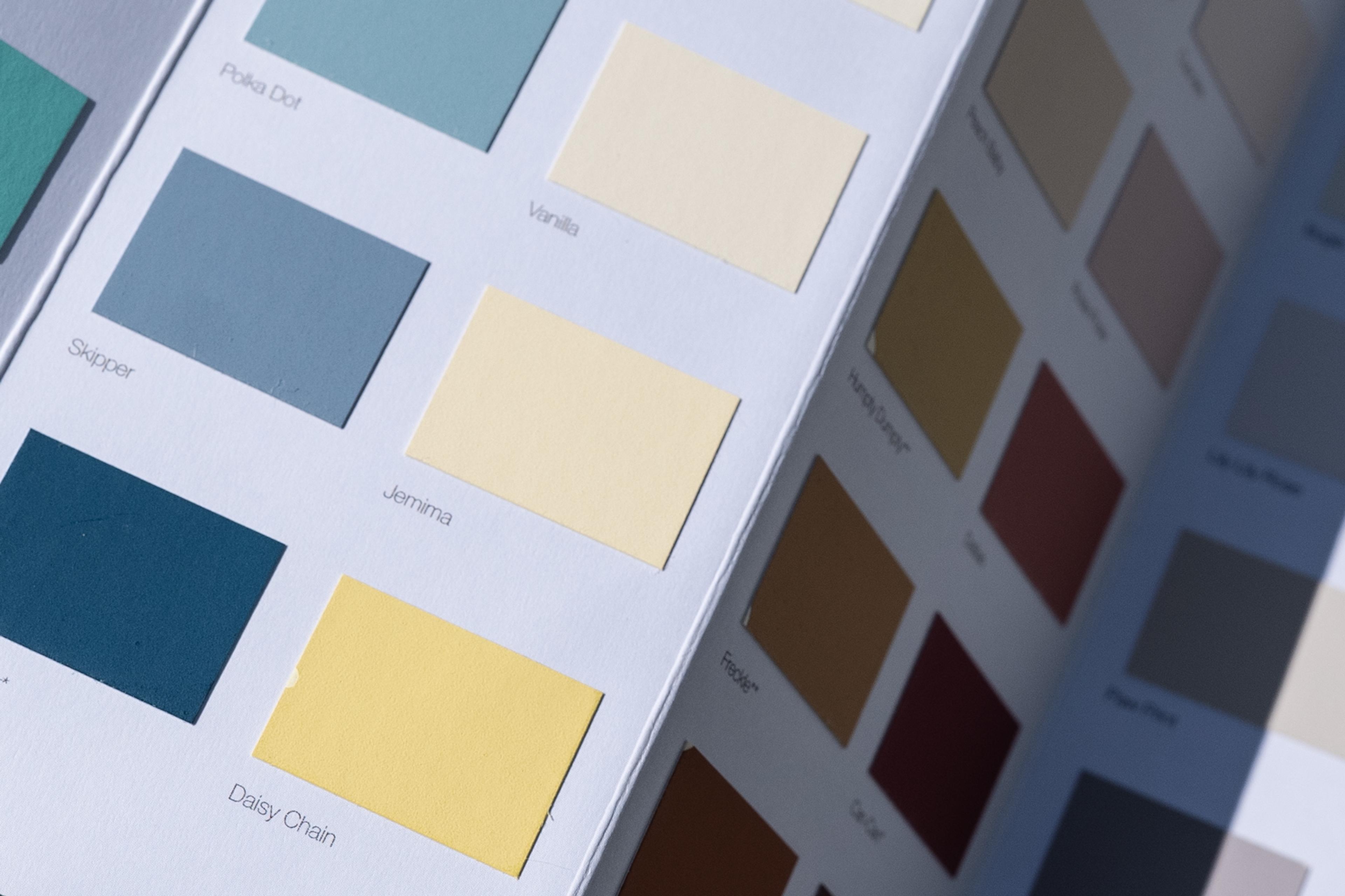 Photo of a paint colour swatch booklet with various shades of blue, yellow and neutral tones in rectangles.
