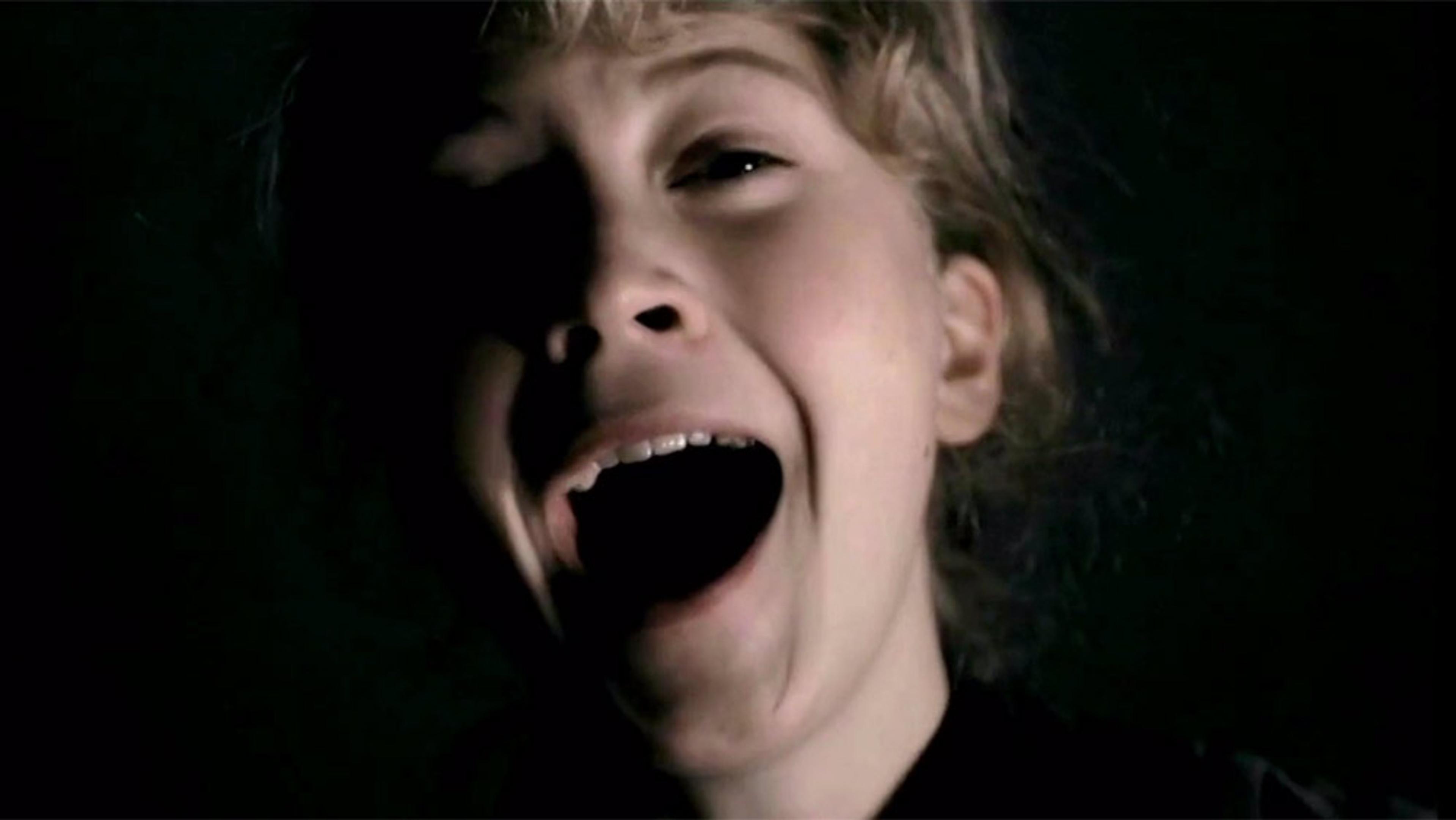 A woman with an open mouth, eyes partially in shadow, and fair hair, appearing to be screaming or yelling in a dark environment.