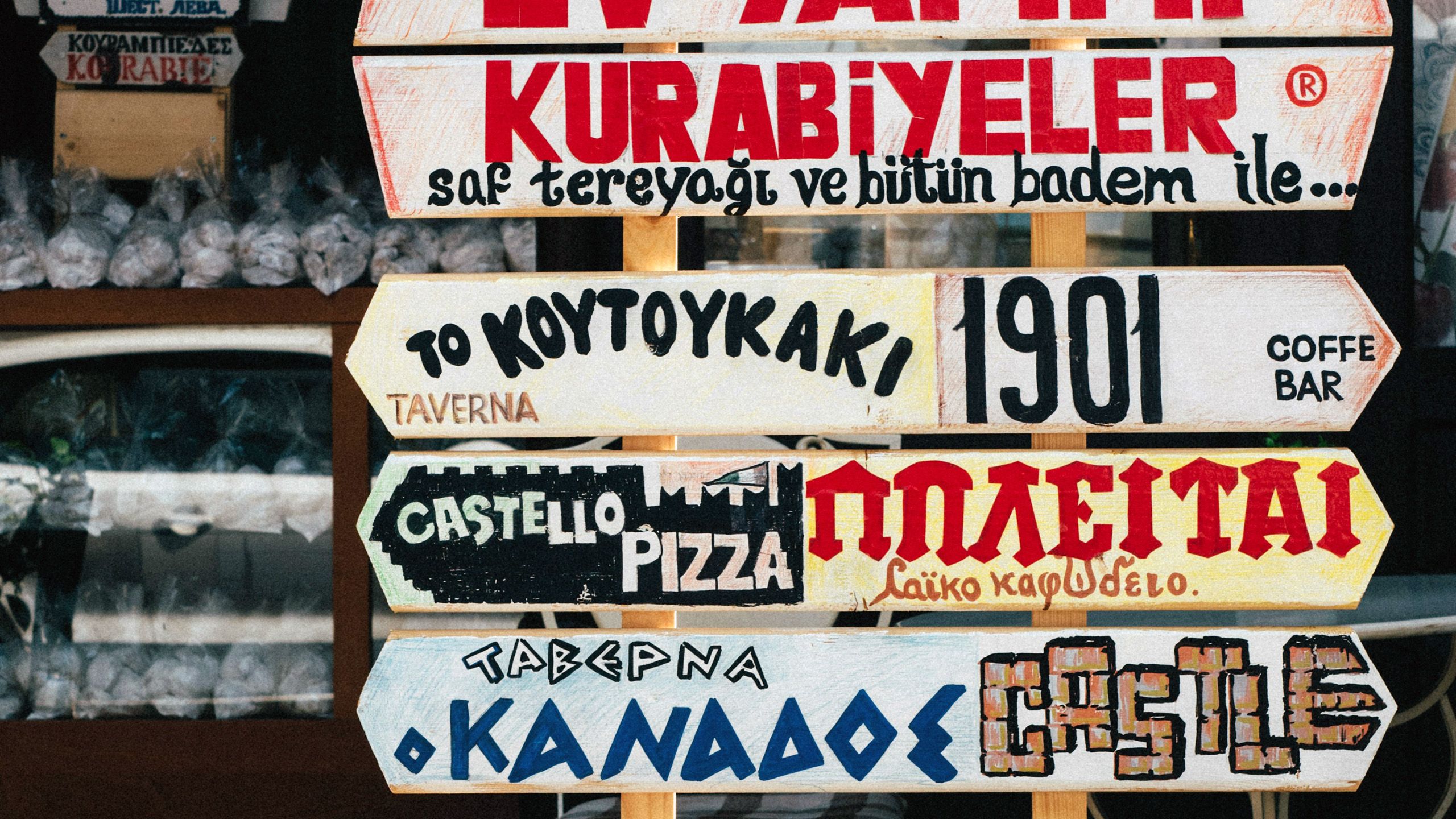 Photo of colourful wooden signs with various text in different languages outside a shop or cafe.