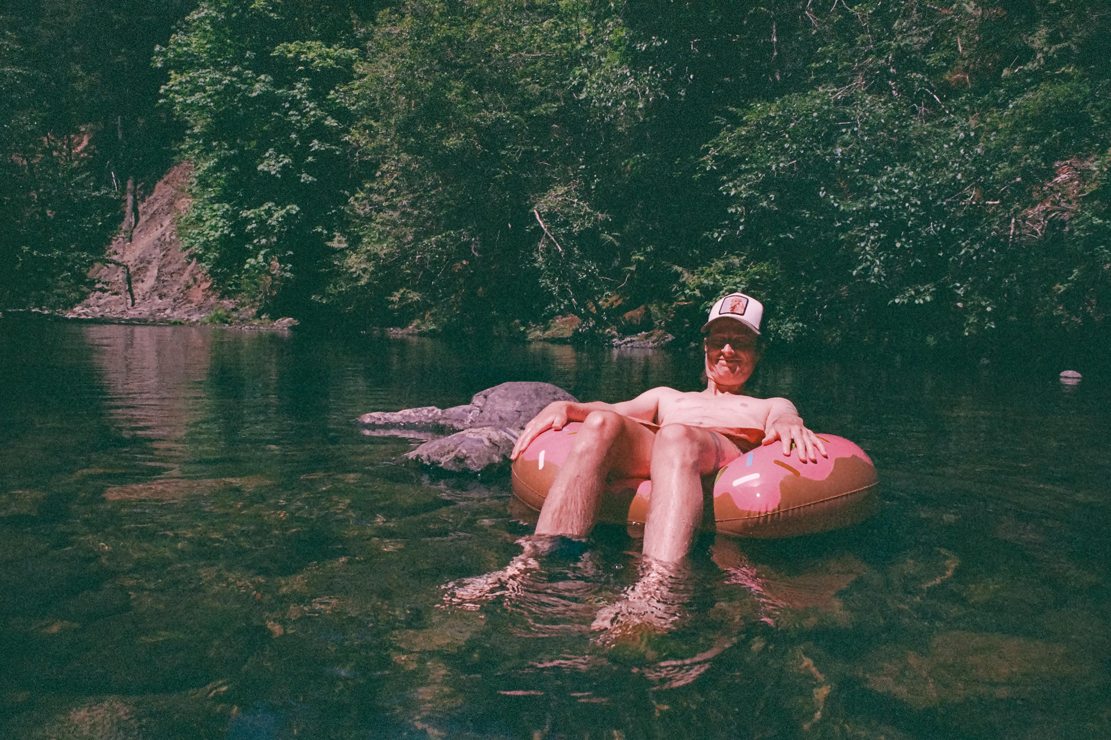 A person relaxing on an inflatable ring in a river surrounded by trees on a sunny day.