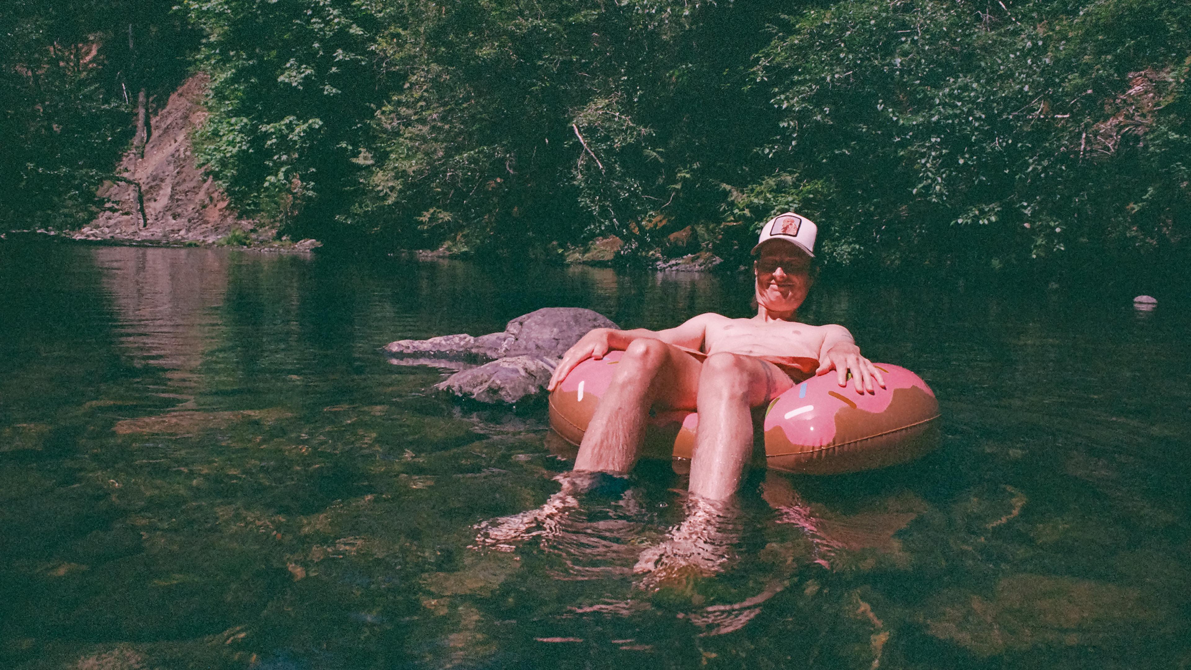 A person relaxing on an inflatable ring in a river surrounded by trees on a sunny day.