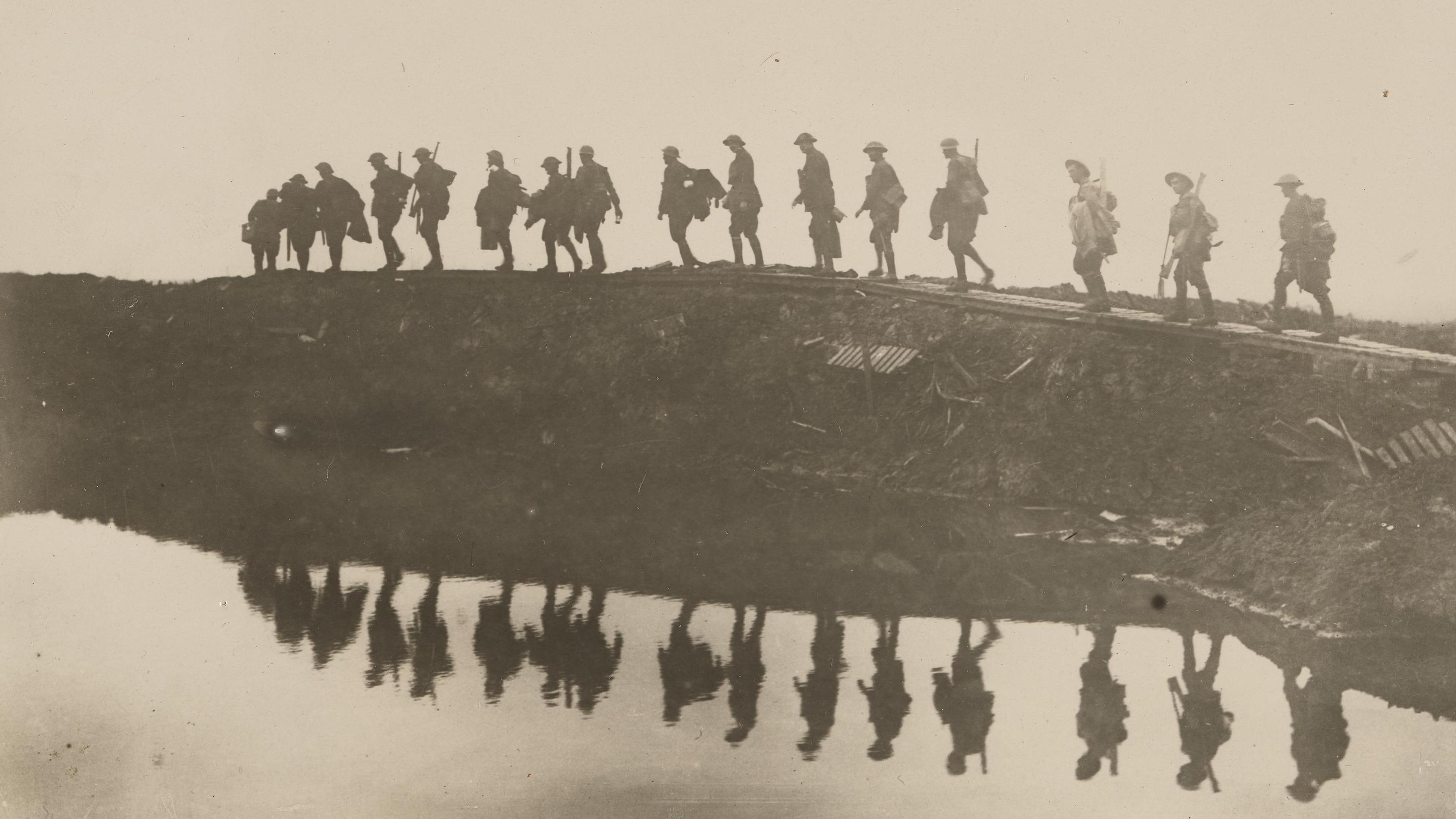 Black and white photo of soldiers walking on a ridge with their reflections in the water below.