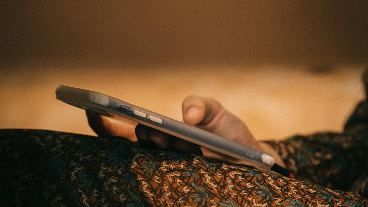 Close-up photo of a person’s hand holding a smartphone with a patterned fabric in the foreground, soft brown background.