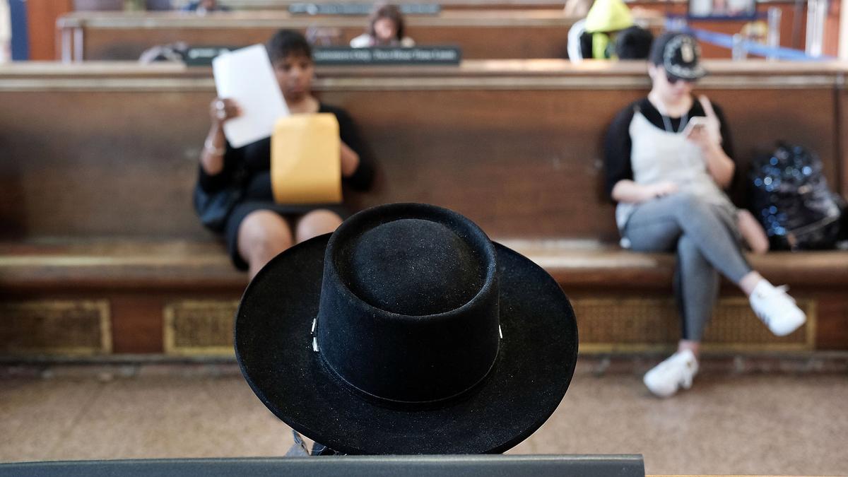 Photo of a waiting room with focus on a black hat. A woman reads papers and another looks at her phone in the background.