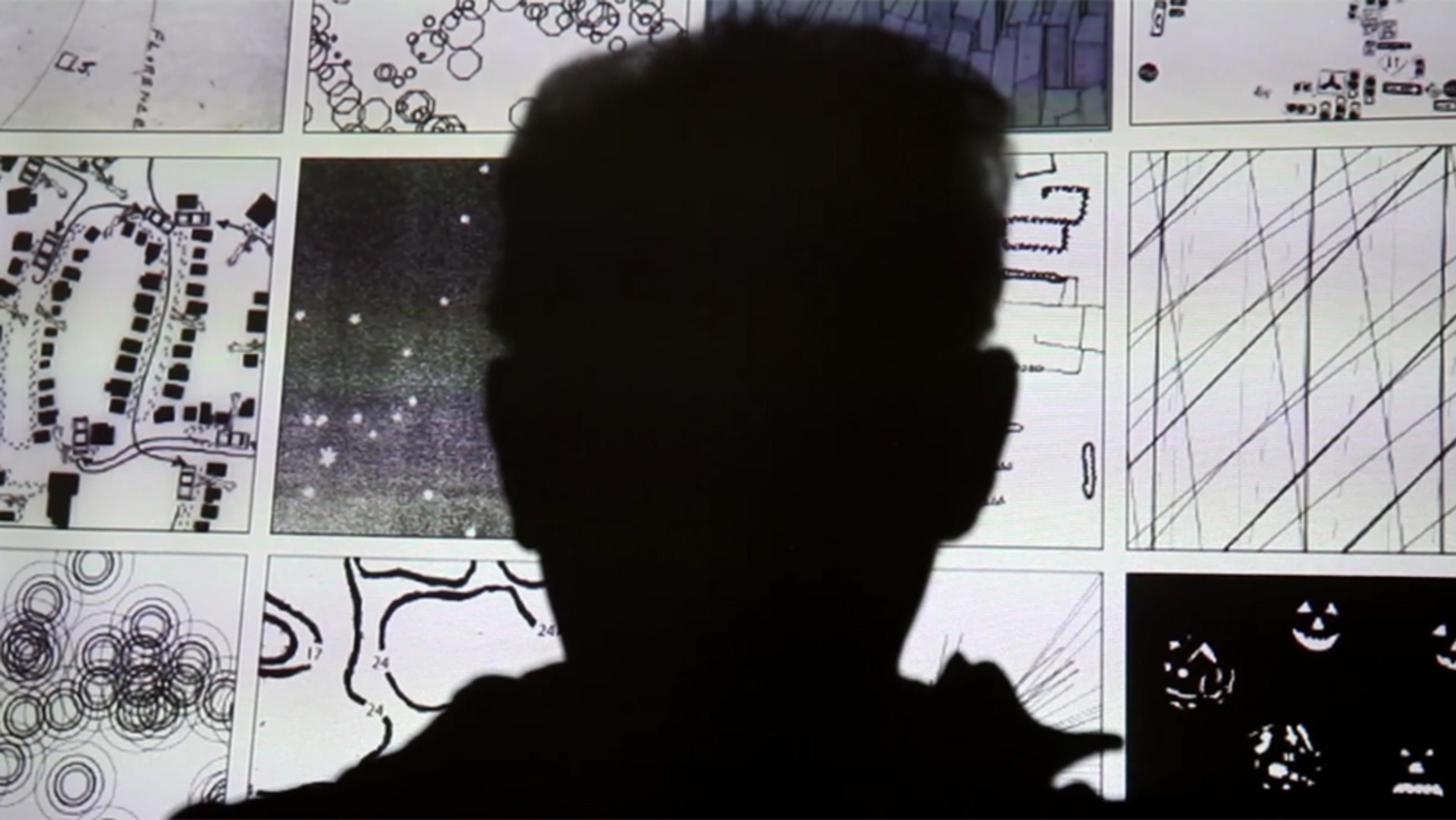 Silhouette of a person against a background of abstract drawings and diagrams on a screen.