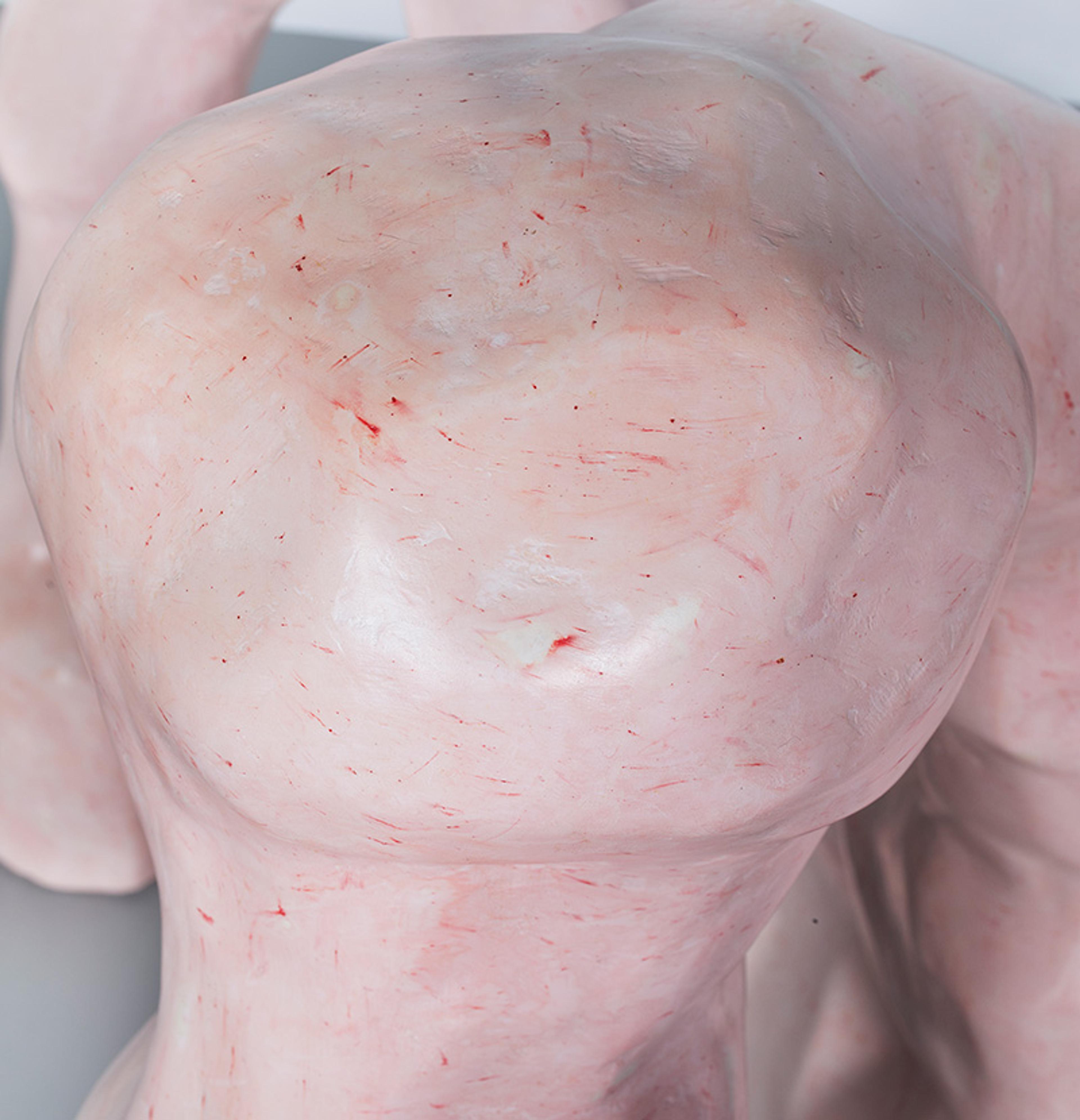 Close-up of a smooth, light-pink sculpture with red streaks on its surface, depicting an abstract human-like form.