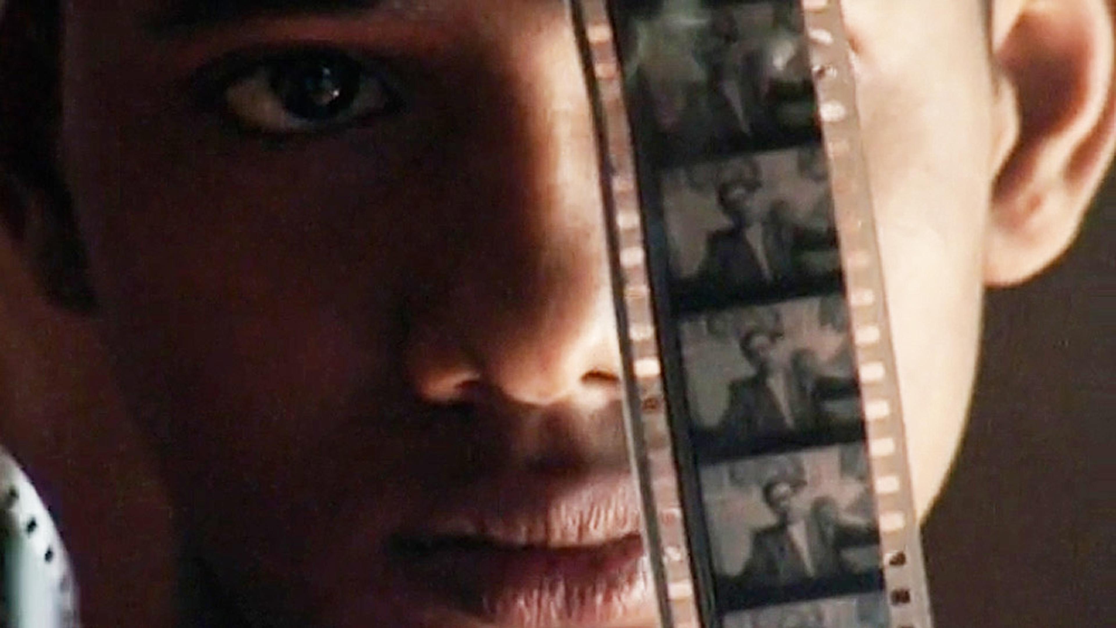 Close-up of a person holding a strip of film negatives, showing their face behind the strip with focus on one eye.