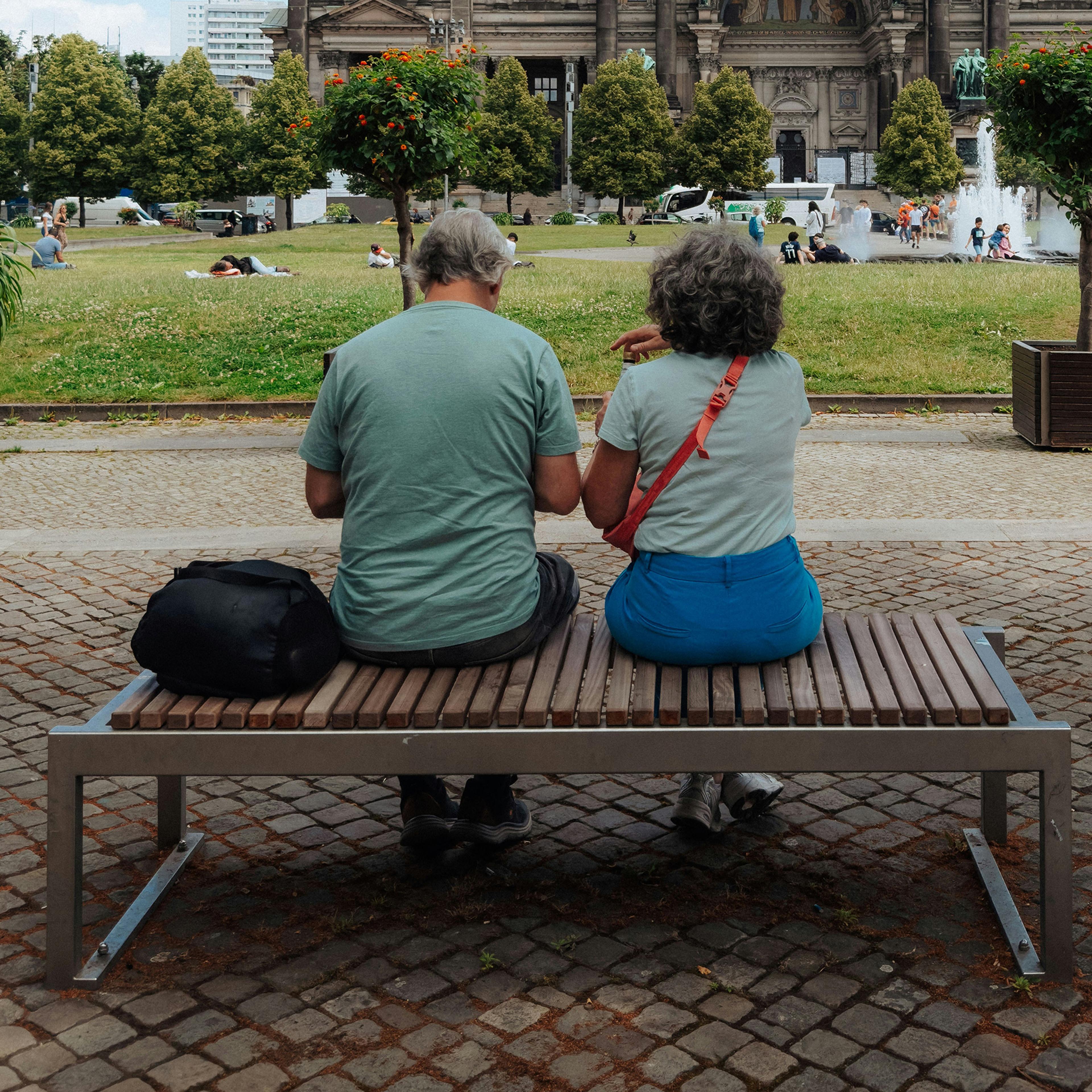 공원 벤치에 앉아 있는 노부부. 배경에는 유서 깊은 건물과 분수가 보인다.<BR>
