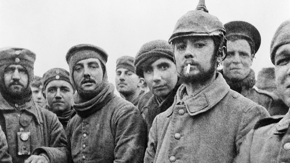 Black and white photo of British and German First World War soldiers wearing winter uniforms and hats, one with a cigarette, looking at the camera.