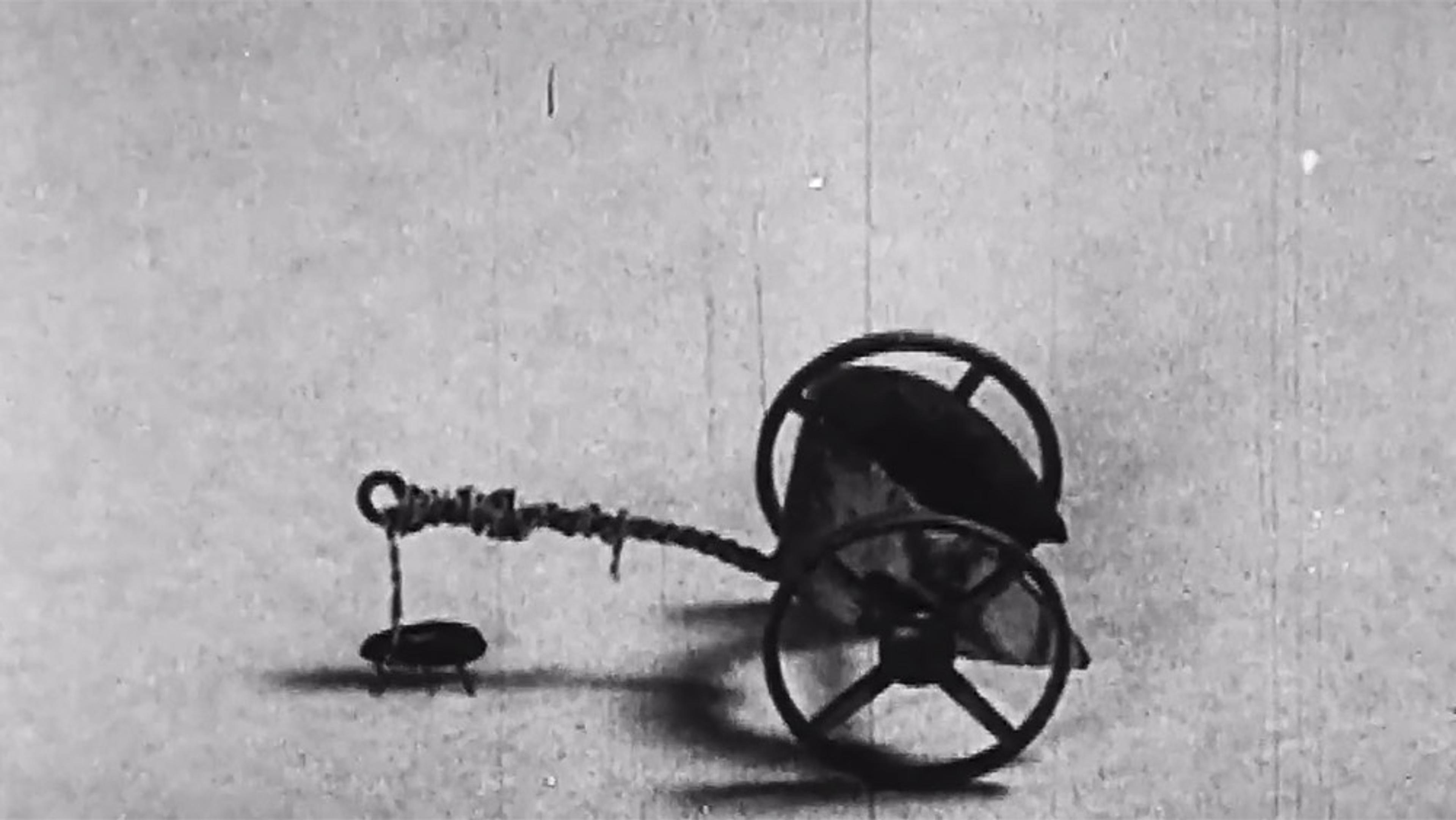 Black and white photo of a vintage toy cart with two large wheels and a long handle on a plain background.