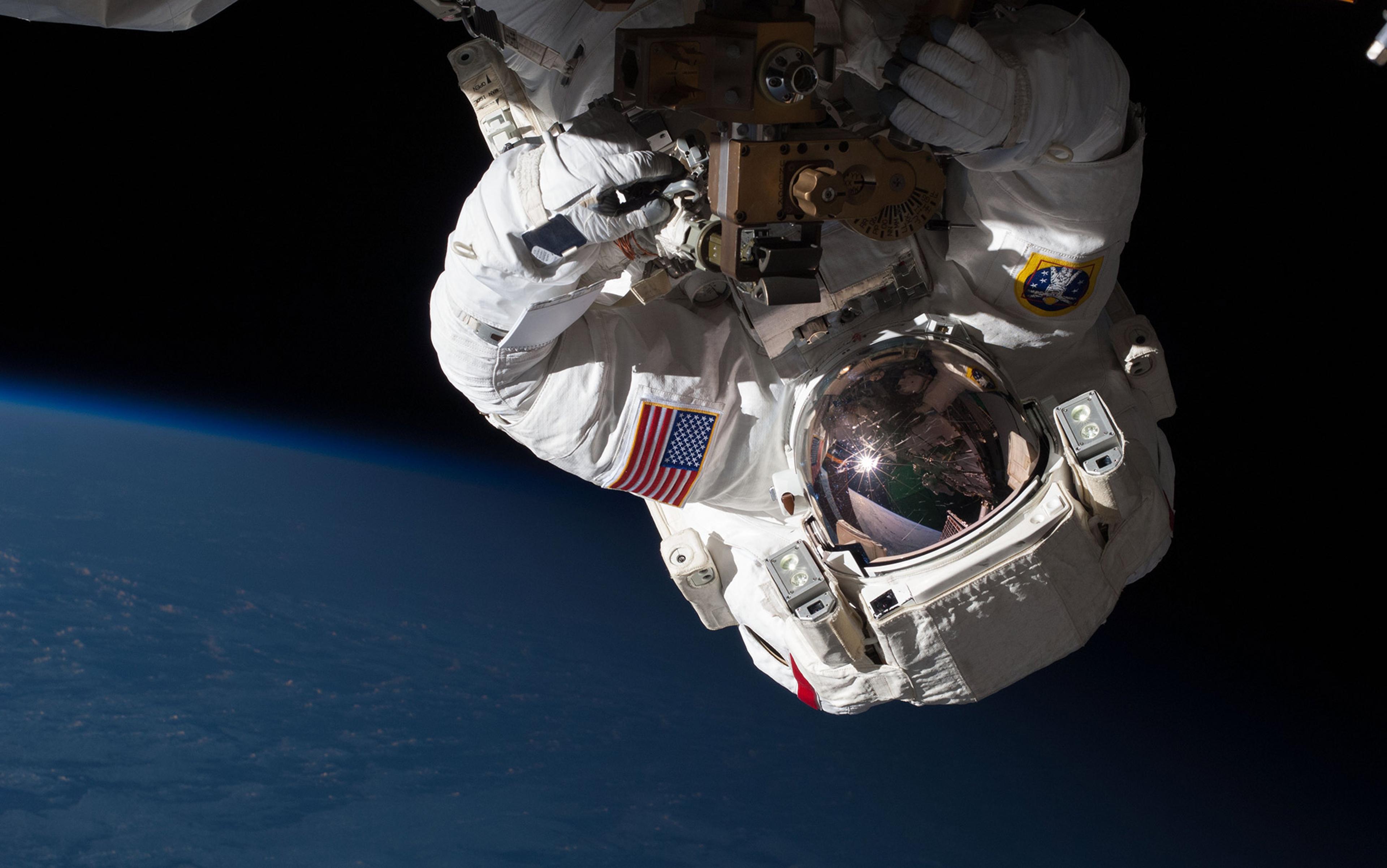 An astronaut in a white spacesuit conducting a spacewalk with Earth, partially illuminated, visible in the background.