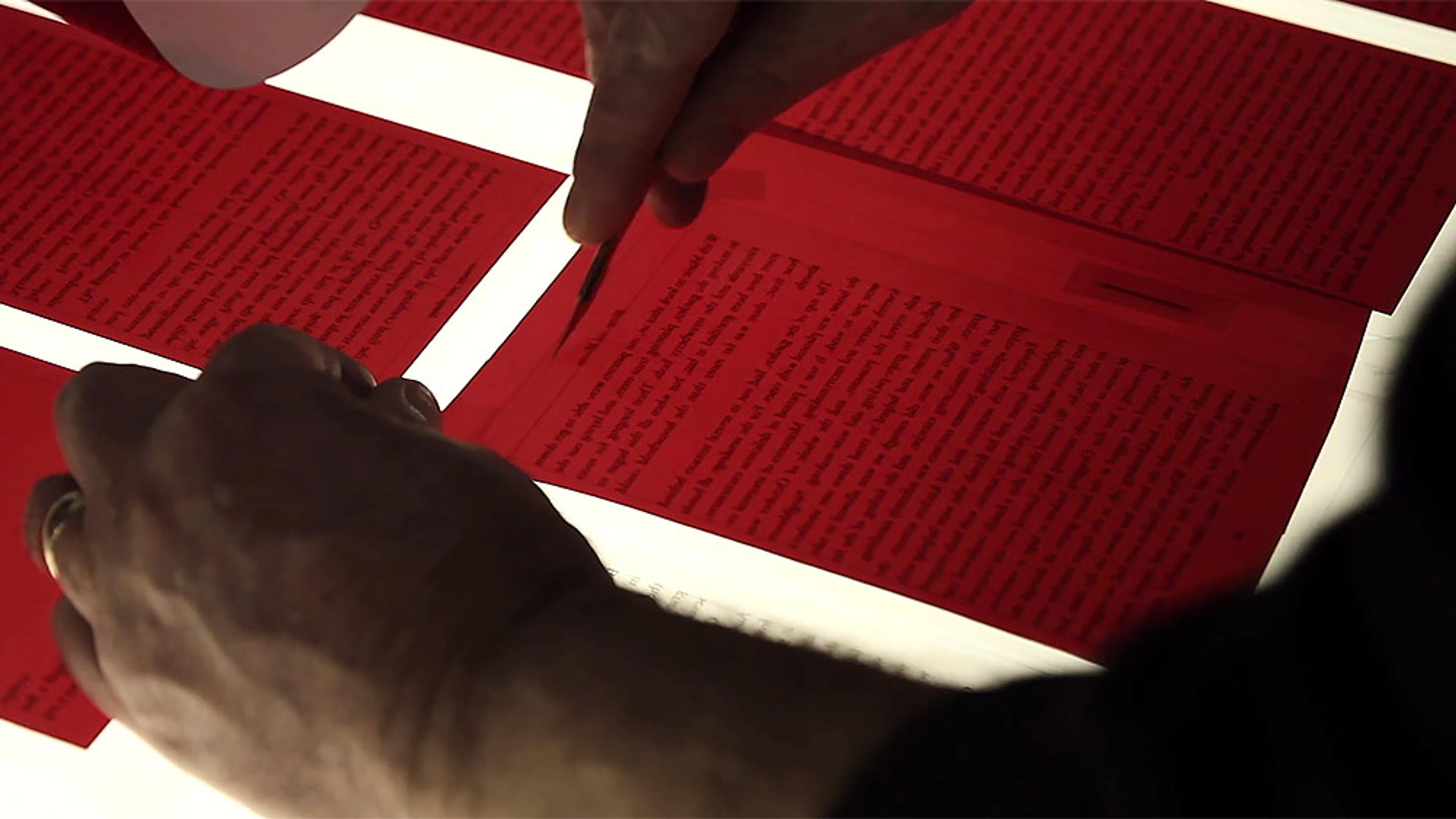 Close-up of hands arranging red text panels on a light table, likely for printing or design purposes.