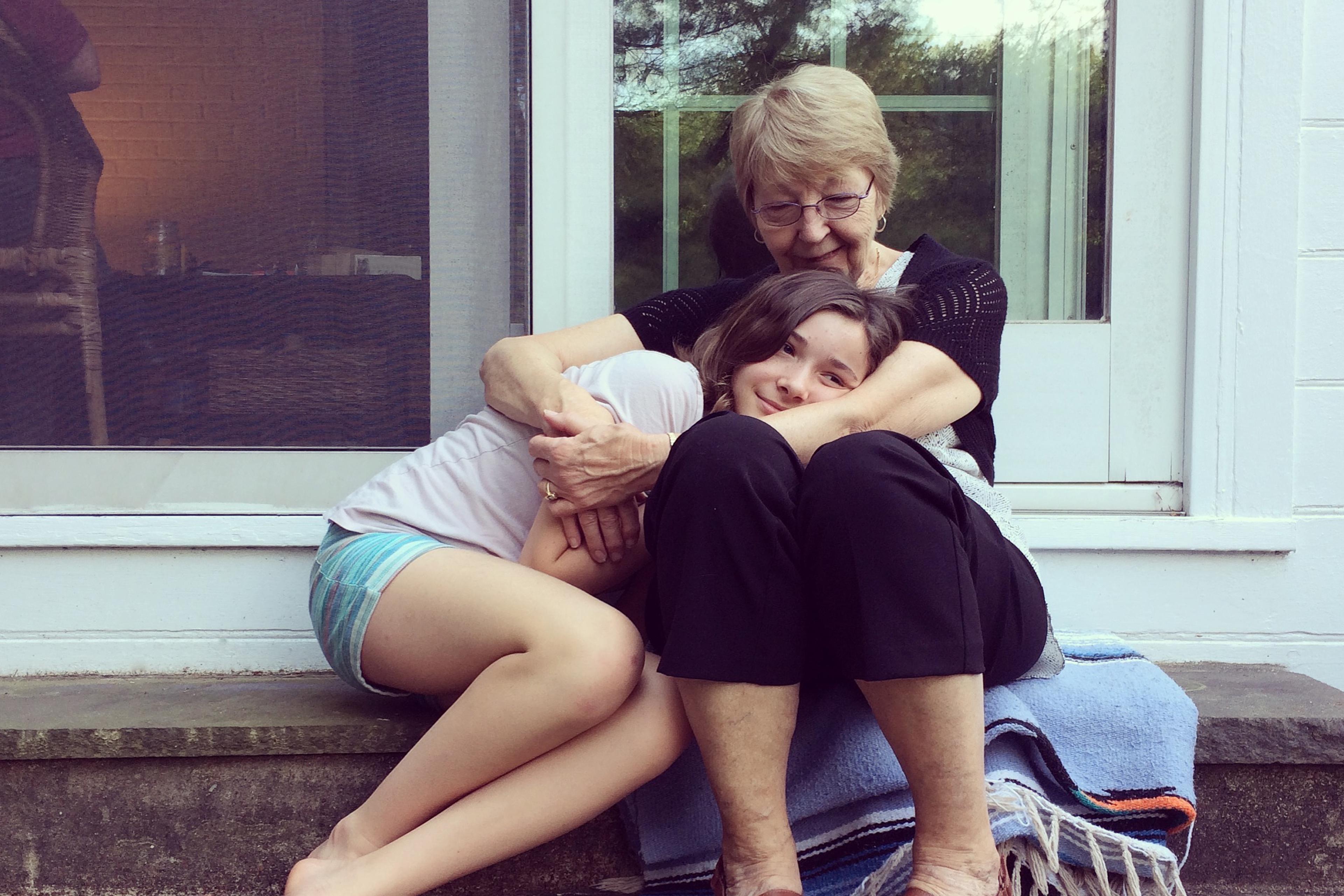 Photo of a woman and girl sitting on steps, embracing affectionately. The girl rests her head on the woman’s lap.