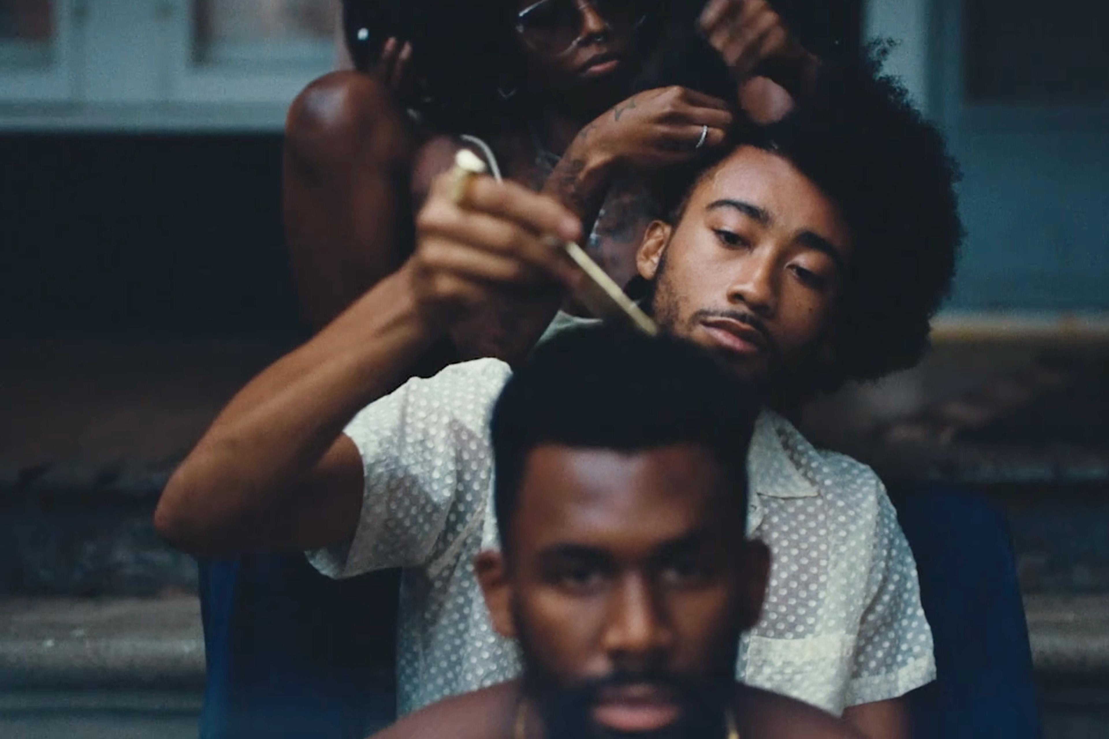 Three people sitting in a line, combing each other’s hair, one holding a comb. The background is slightly blurred.