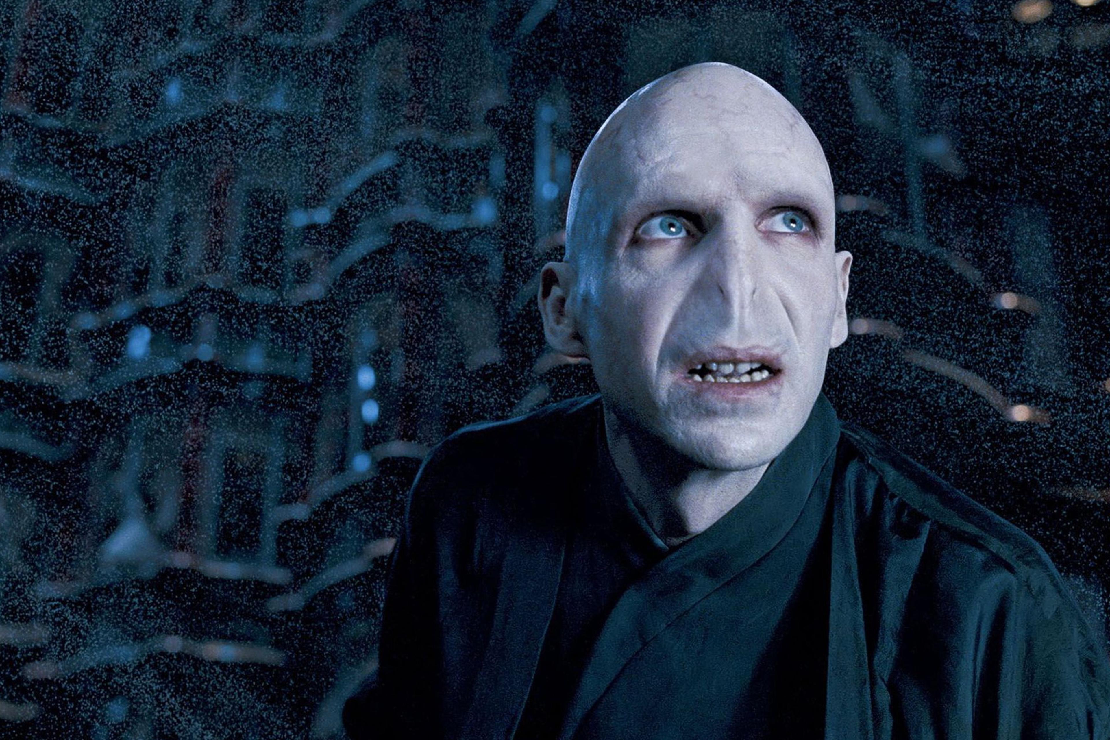 A fictional character with pale skin and no nose looks up in a dim, atmospheric setting, photo from a film scene.