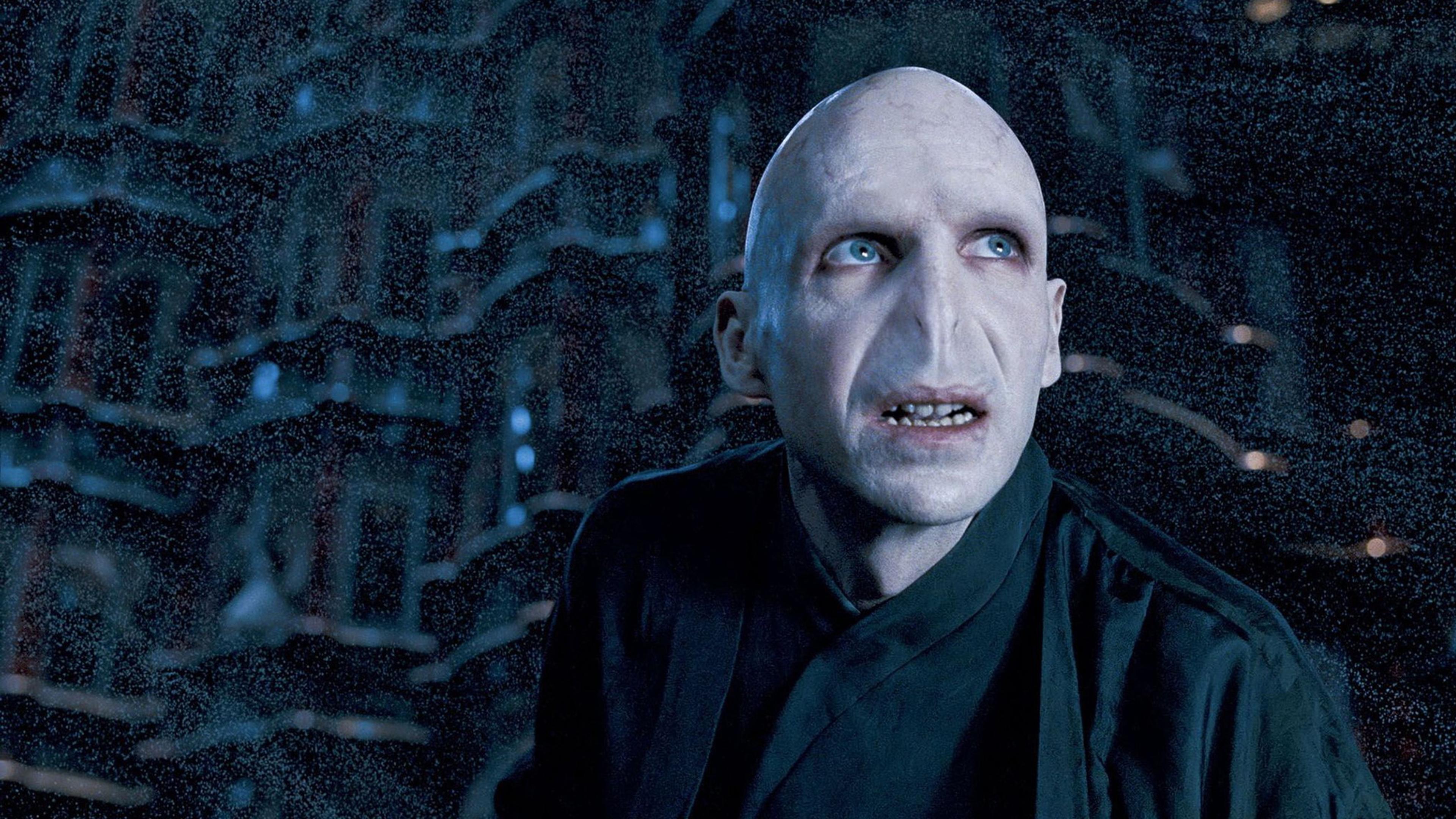 A fictional character with pale skin and no nose looks up in a dim, atmospheric setting, photo from a film scene.