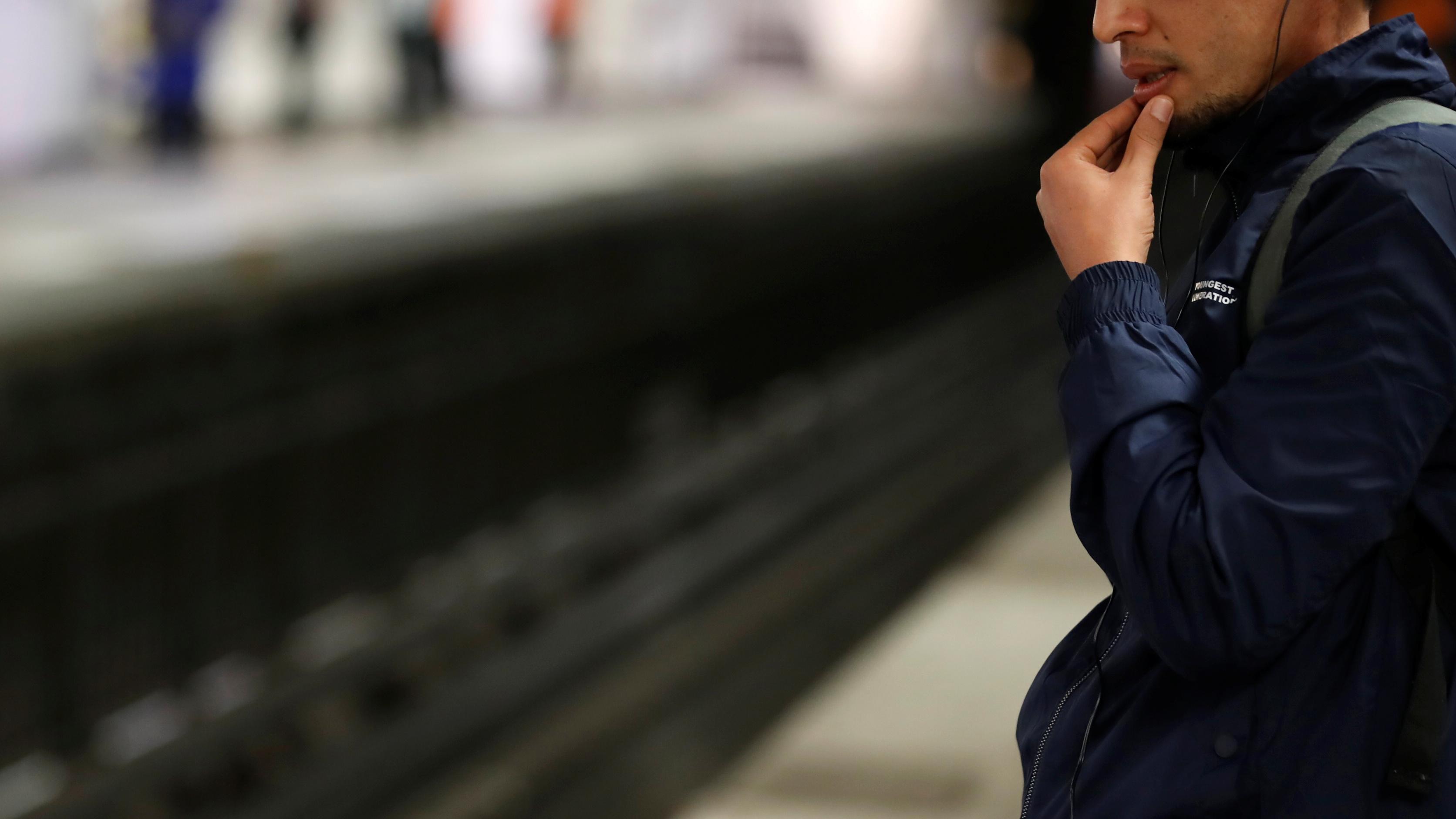 Photo of a person in a blue jacket standing on a train platform, staring at the tracks in a thoughtful pose.